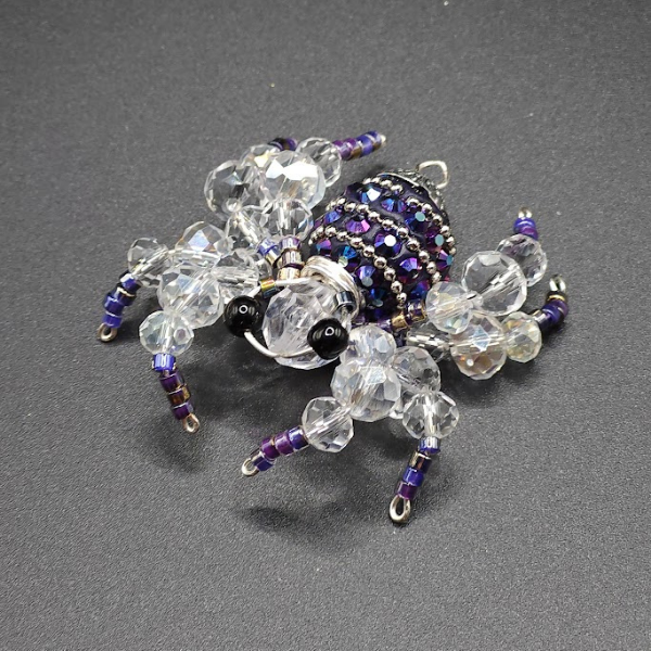 Beaded spider jewelry made of clear, purple, and black beads on a dark surface.