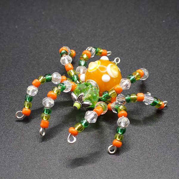 Beaded spider with orange, green, clear, and yellow beads on a black background.