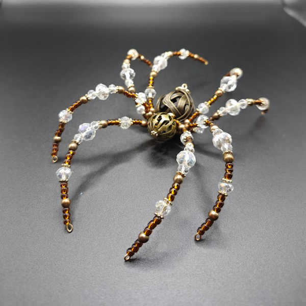 Beaded spider ornament with metallic and clear beads on a dark surface.