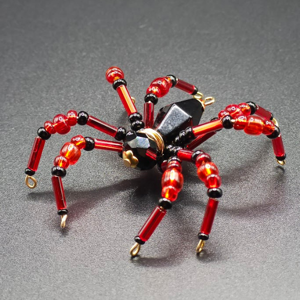 Beaded spider jewelry with black, red, and gold accents on a dark surface.