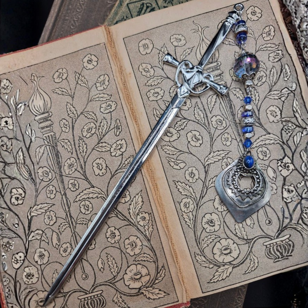 A decorative open book with floral patterns, a silver sword bookmark on top of it.