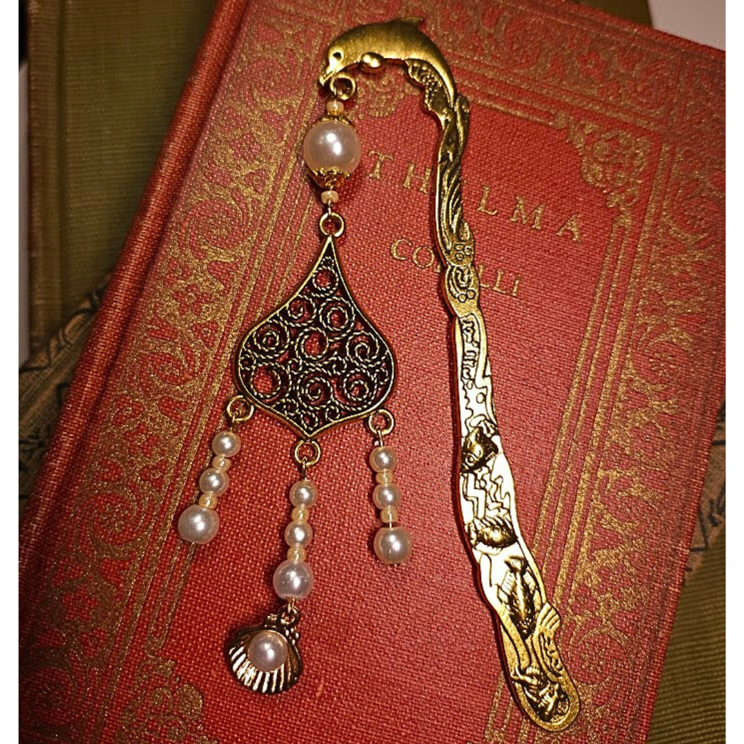 An ornate bookmark with pearls and gold design placed on a red, gold-embossed book cover.