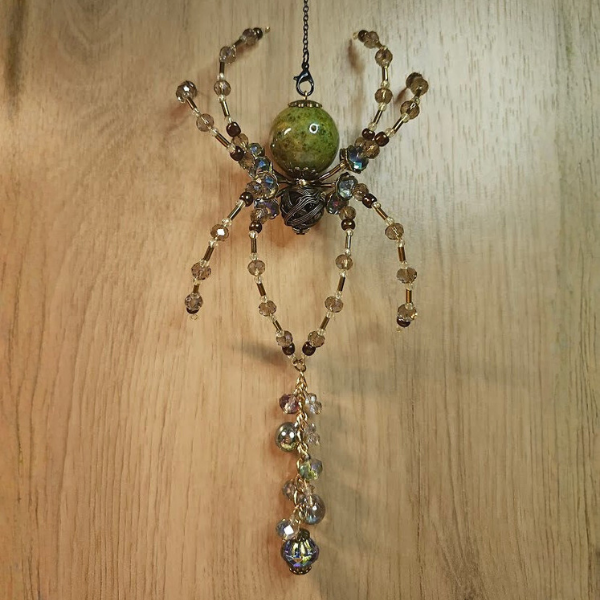 A spider-shaped ornament made of beads and a green central bead with hanging crystal-like decorations, hanging from a black chain.