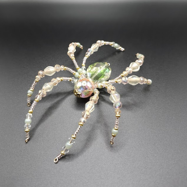 Beaded bracelet in the shape of a spider with bead legs and a large bead body, placed on a dark surface.