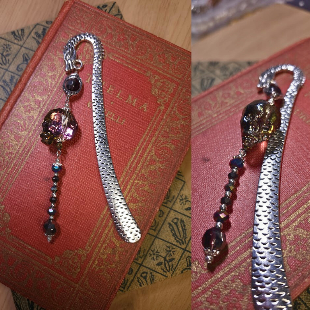 A decorative bookmark with a skull-shaped charm, black and purple beads, and a silver chain, resting on a red and gold book cover.