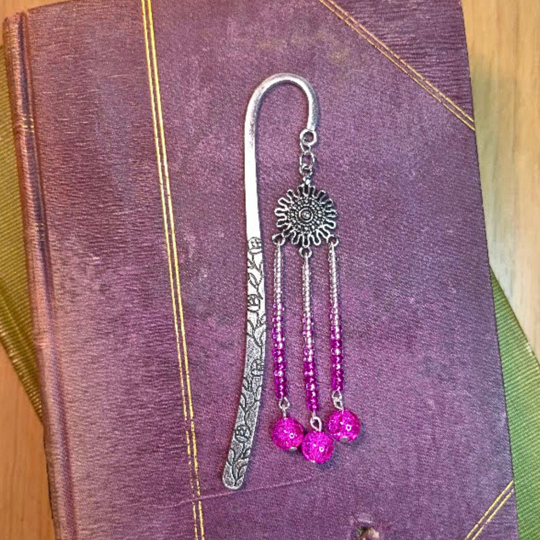 A decorative bookmark with a chain and chain tassels with pink beads, resting on a textured purple book cover.
