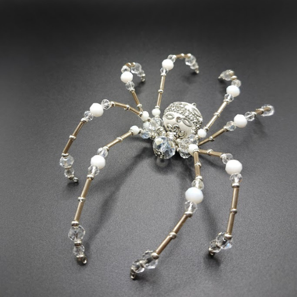Decorative spider ornament with a silver beaded body and clear and white beaded legs, placed on a black surface.