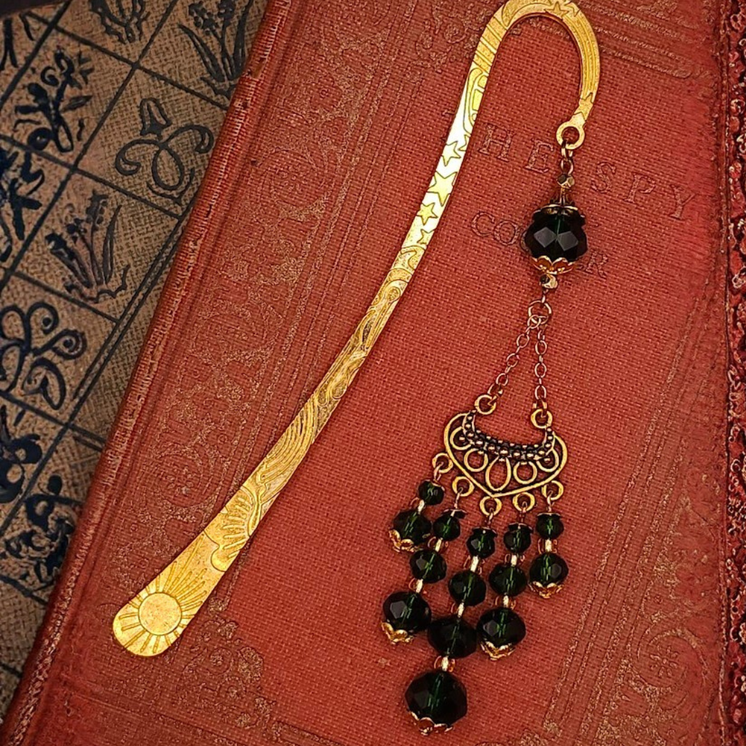 An ornate vintage gold-tone bookmark and a black beaded charm with gold accents resting on a red textured book cover.