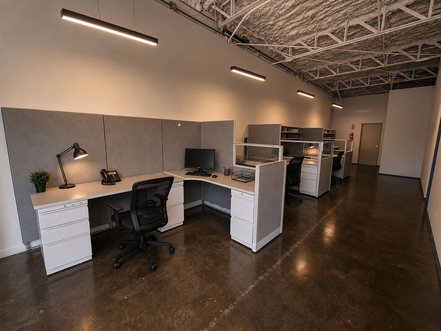 Empty modern office with cubicles, desks, black chairs, laptops, desk lamps, a potted plant, and overhead lighting.