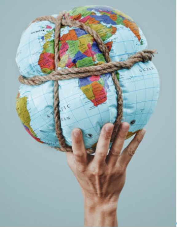A person's hand holding a deflated inflatable world globe wrapped with a brown rope.