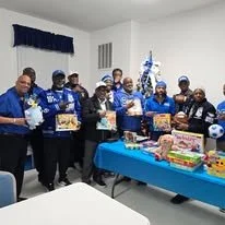 Fraternity brothers standing behind a table with toys and gifts, at a Christmas holiday toy drive.