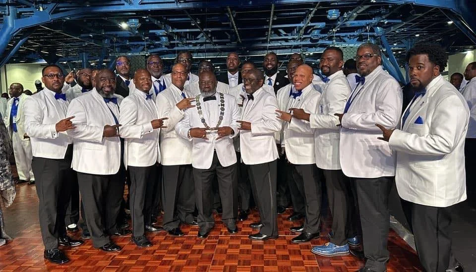 Phi Beta Sigma men dressed in white tuxedos with blue bow ties, standing together at the fraternity Orchid Ball.
