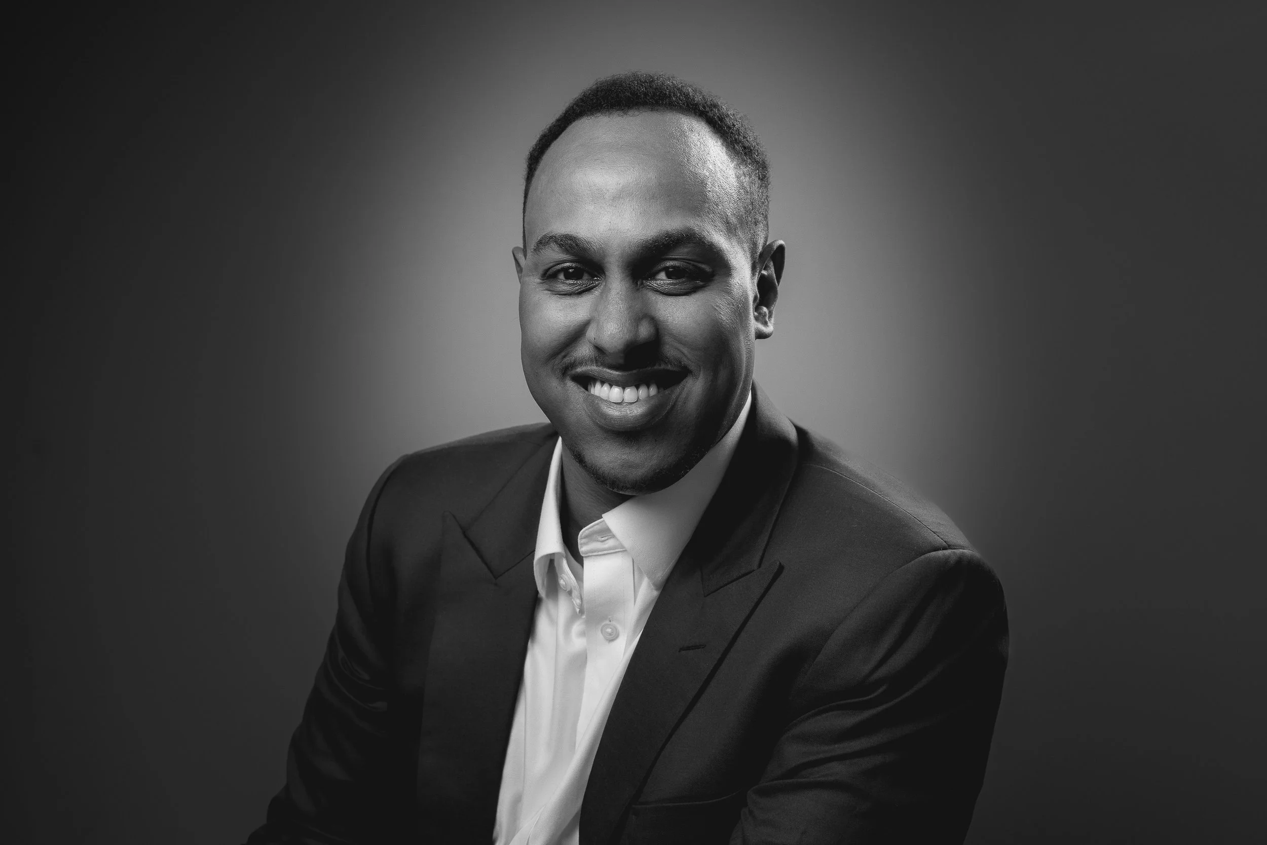Black and white portrait of a smiling man wearing a suit and white shirt, posing against a plain background.