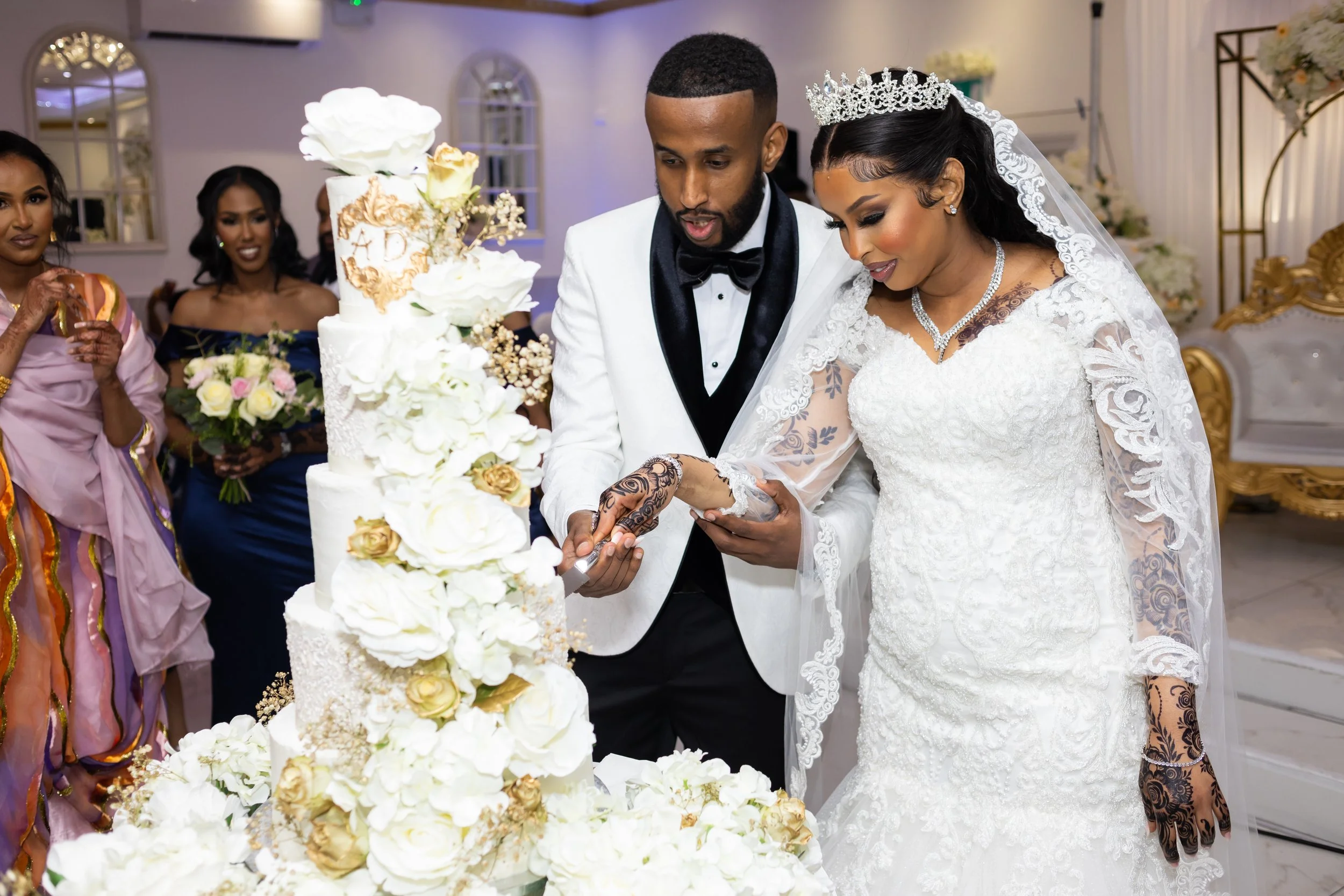 A bride and groom cutting their wedding cake together at a wedding reception, surrounded by guests and elegant decorations.