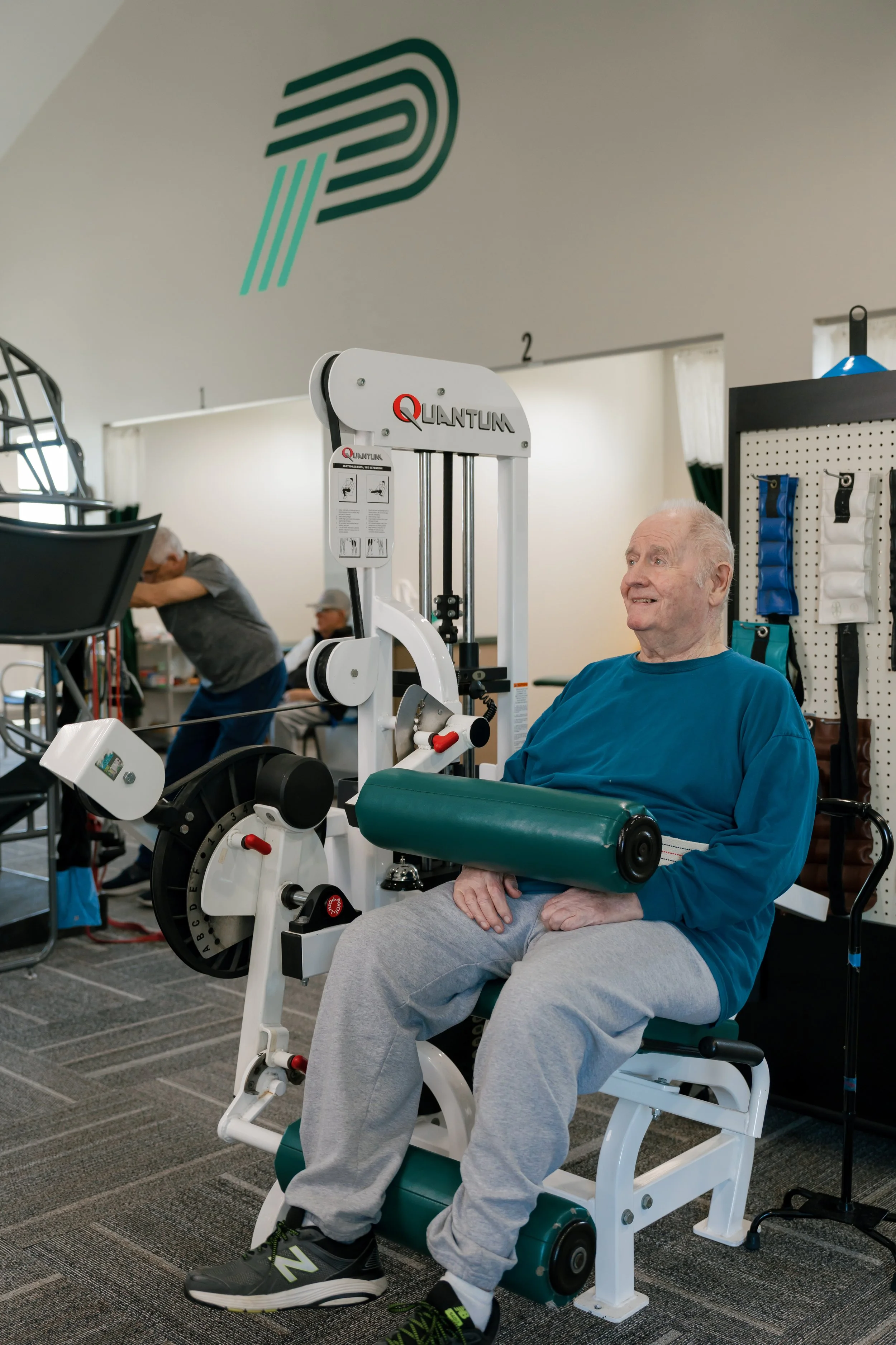 Older man using a seated leg extension machine in a rehabilitation gym