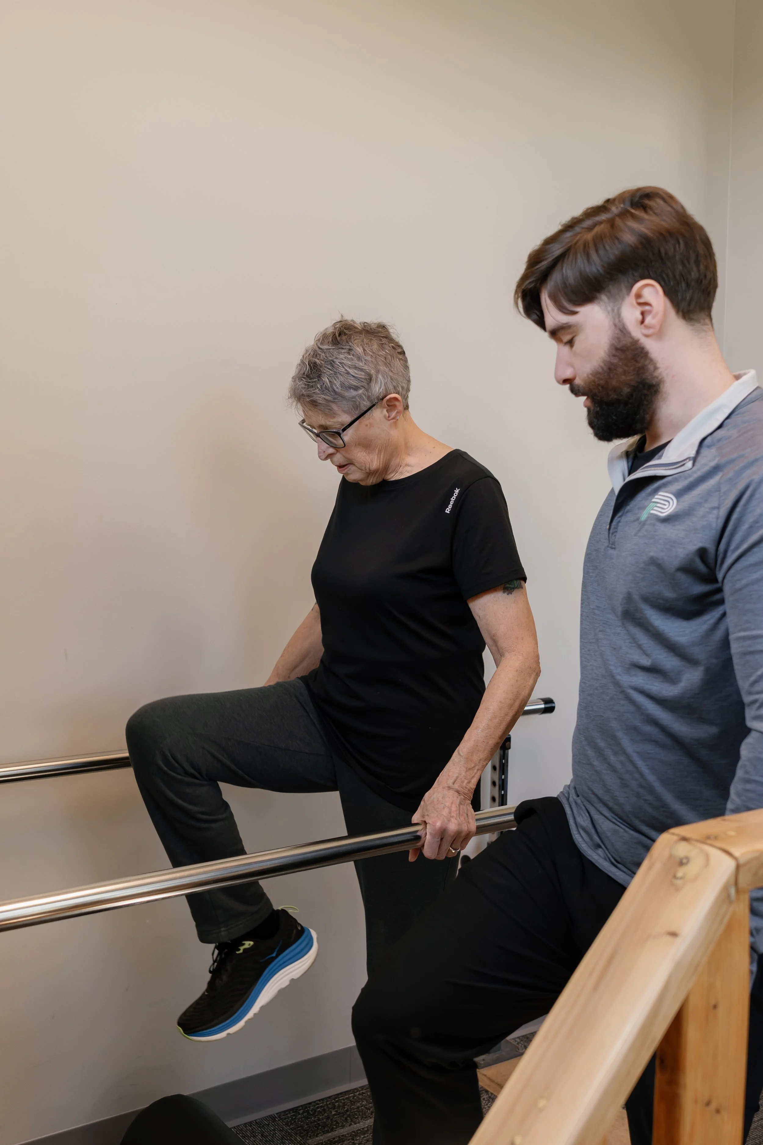 Older woman performing a seated leg exercise with a therapist in a rehabilitation gym.