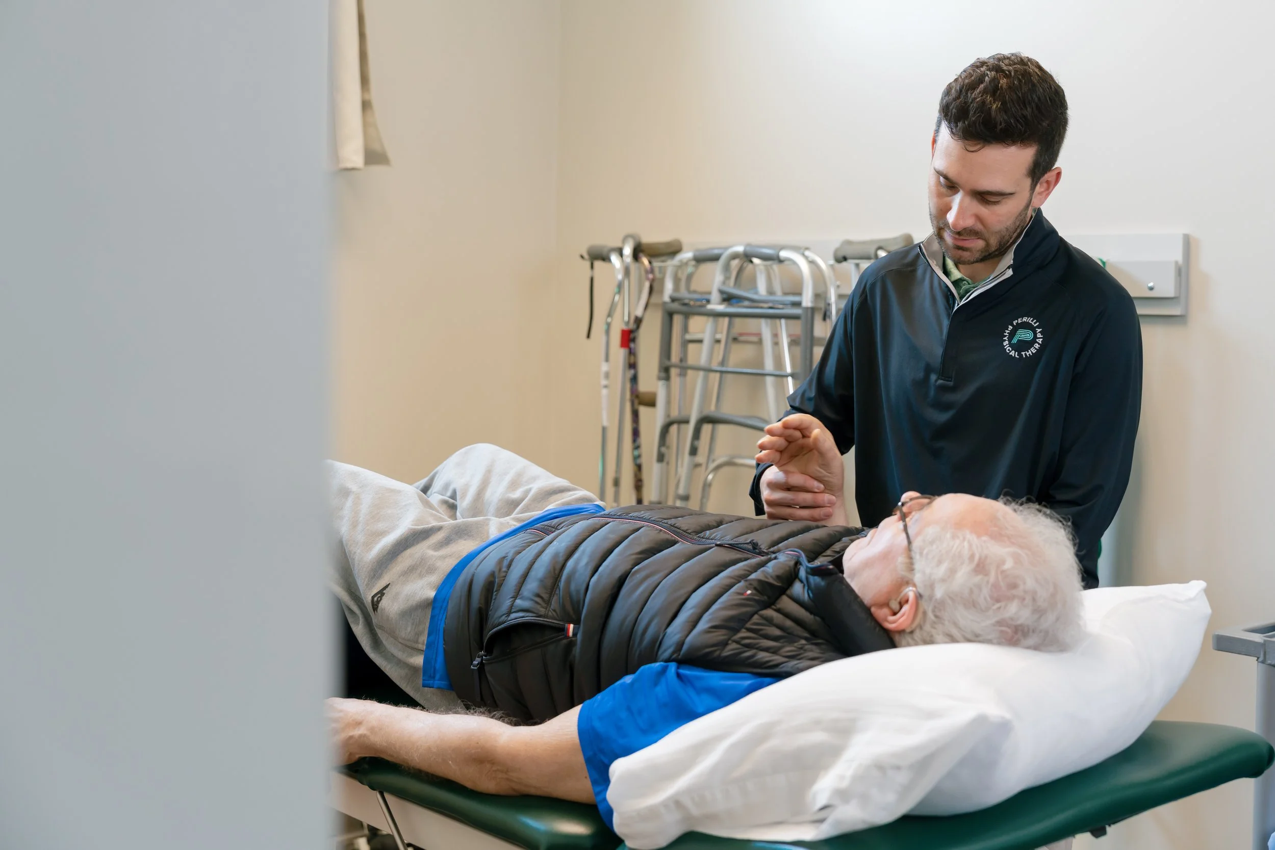 Physical therapist assisting an older man lying on a treatment table in a clinic