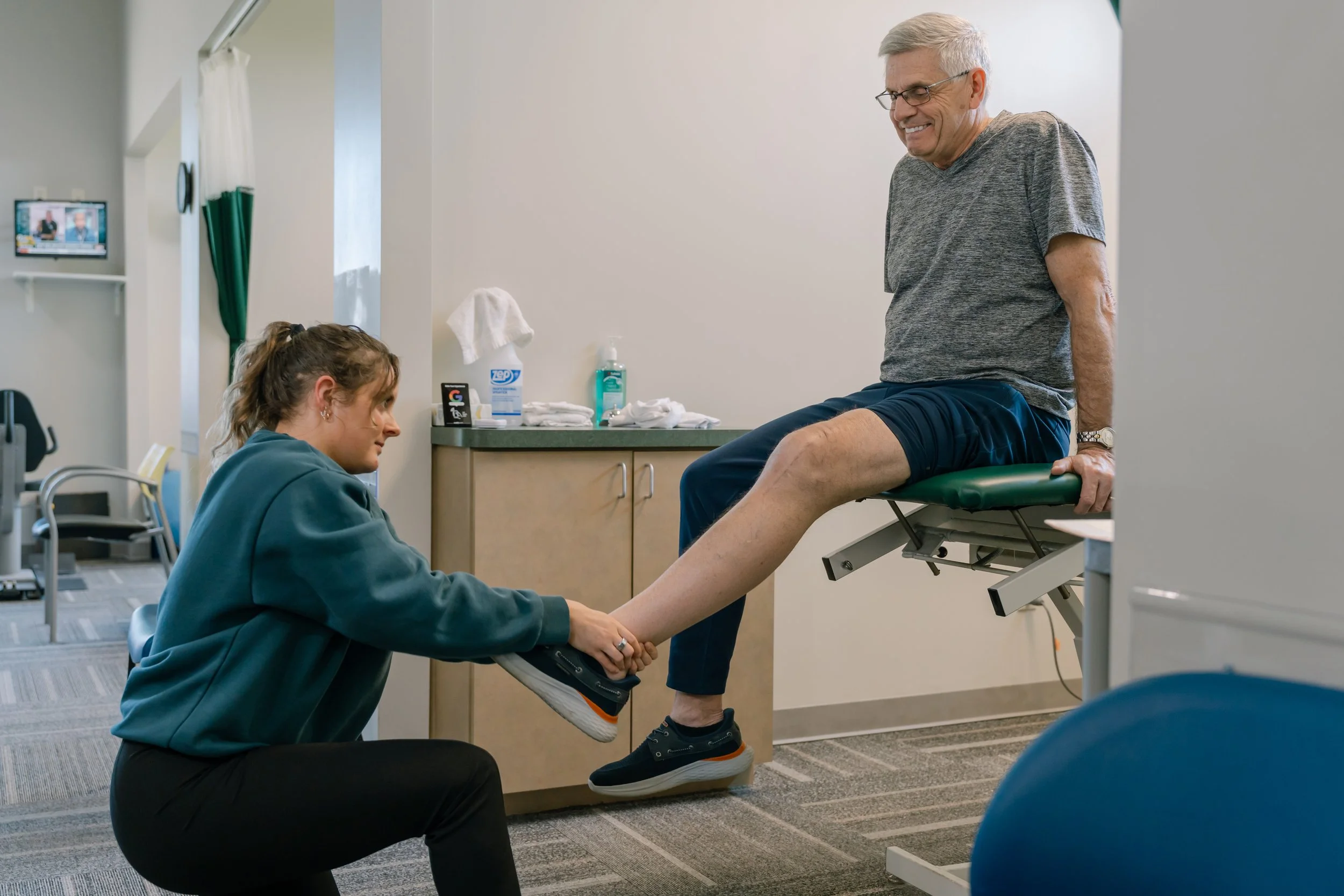 Physical therapist assisting an older man with a leg exercise in a clinic