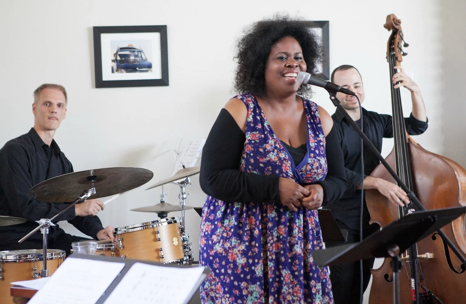 A jazz band performing with a woman singing into a microphone, a drummer, and a double bass player.
