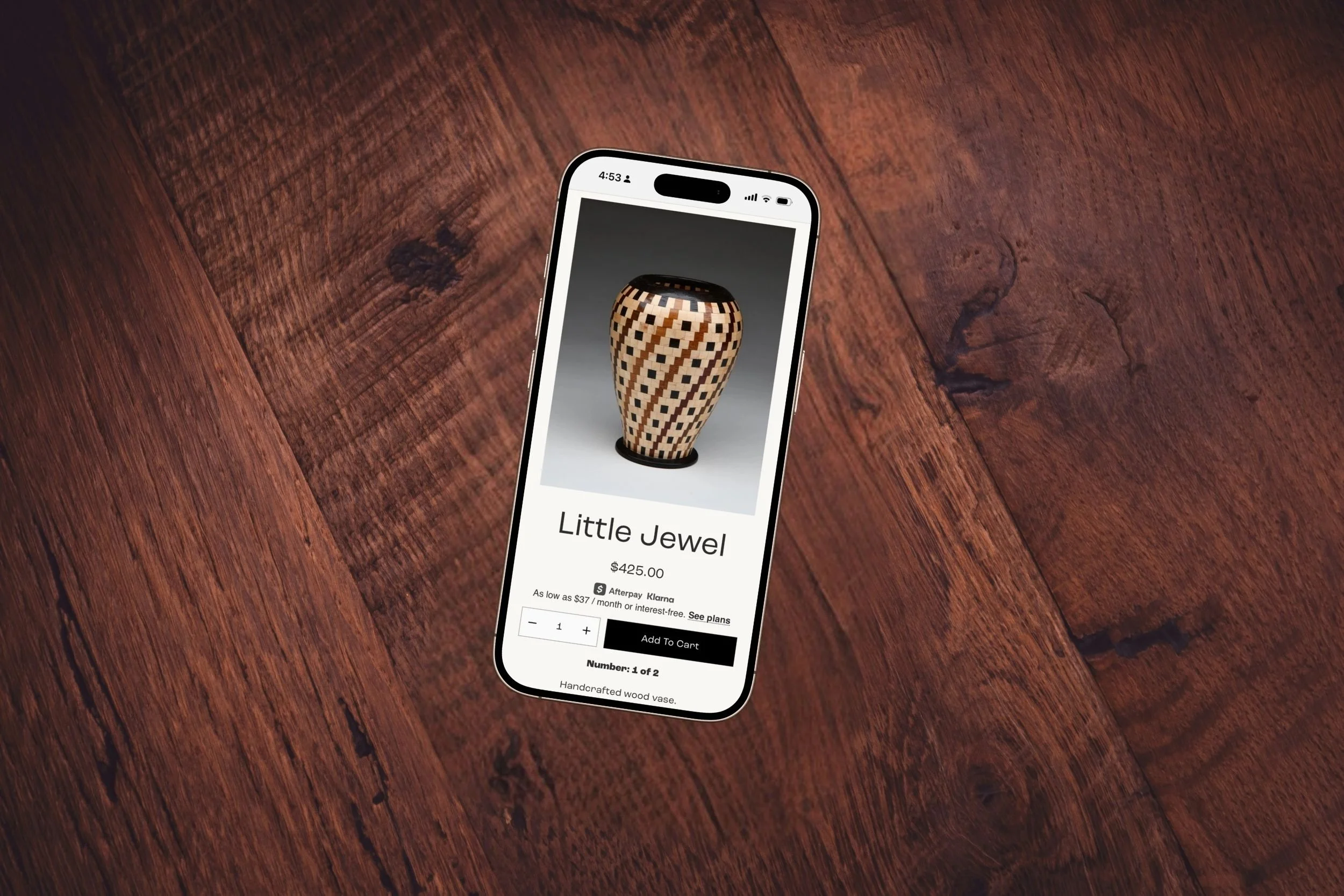A smartphone displaying an online product listing for a handcrafted wood vase called 'Little Jewel,' priced at $425, on a wooden table.