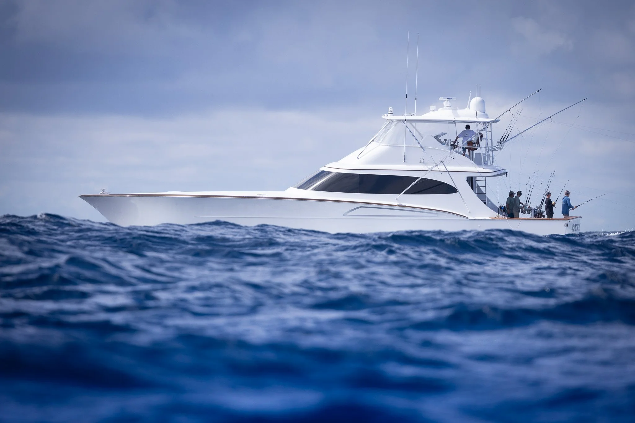 A white yacht with four people on board, fishing in the ocean under cloudy skies.