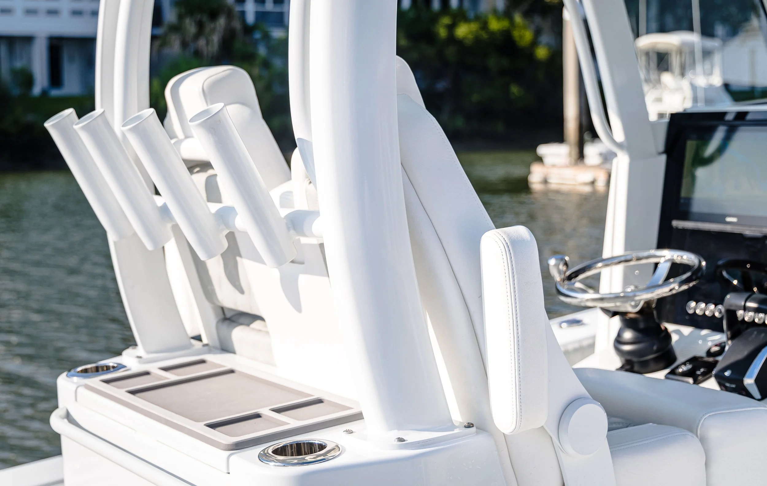 Close-up of the helm and white cushioned seats on a luxury boat, with water and green trees in the background.
