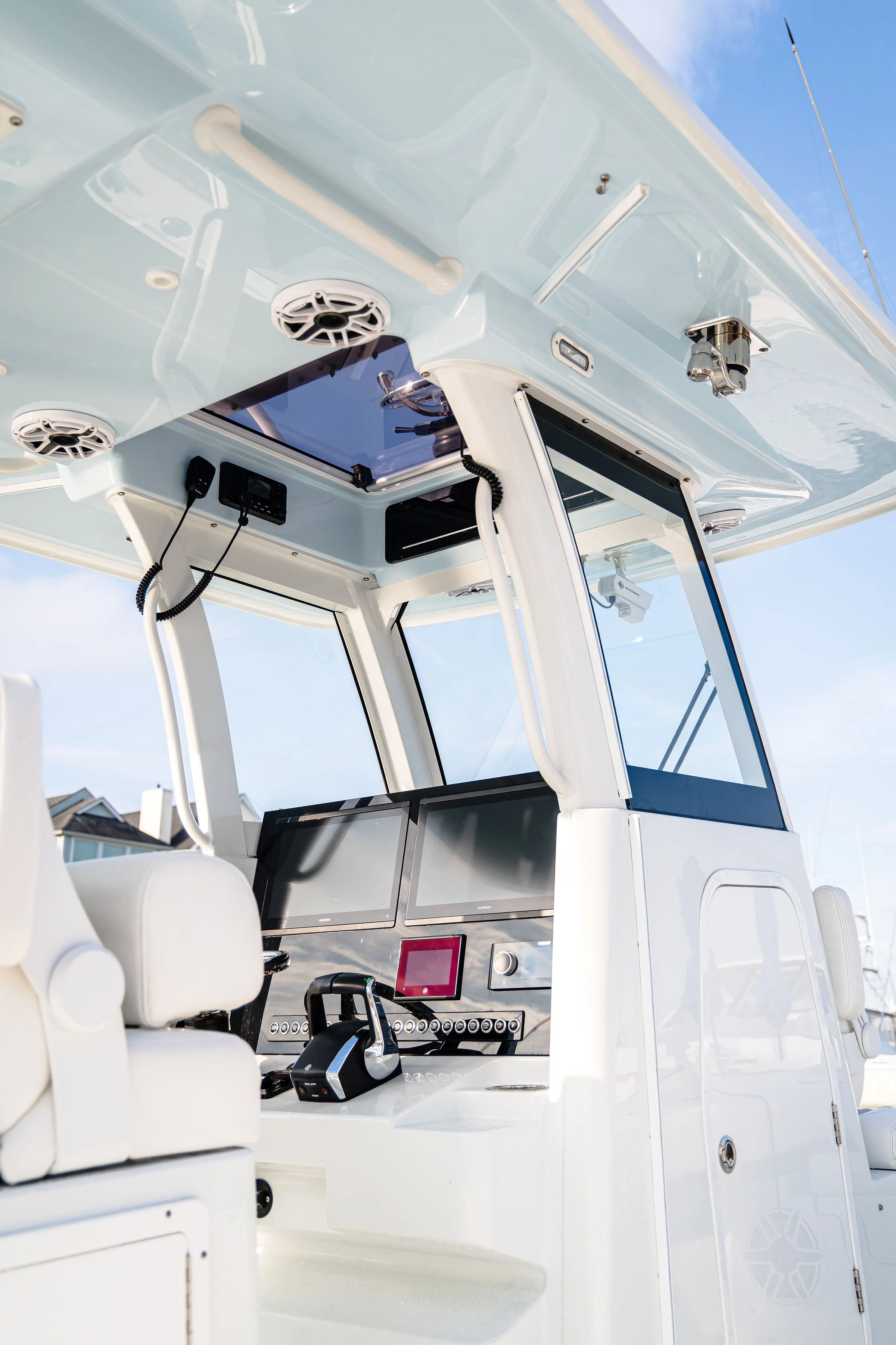 View of the cockpit of a white yacht, showing a steering wheel, multiple screens, communication devices, speakers, and control panels under a clear blue sky.
