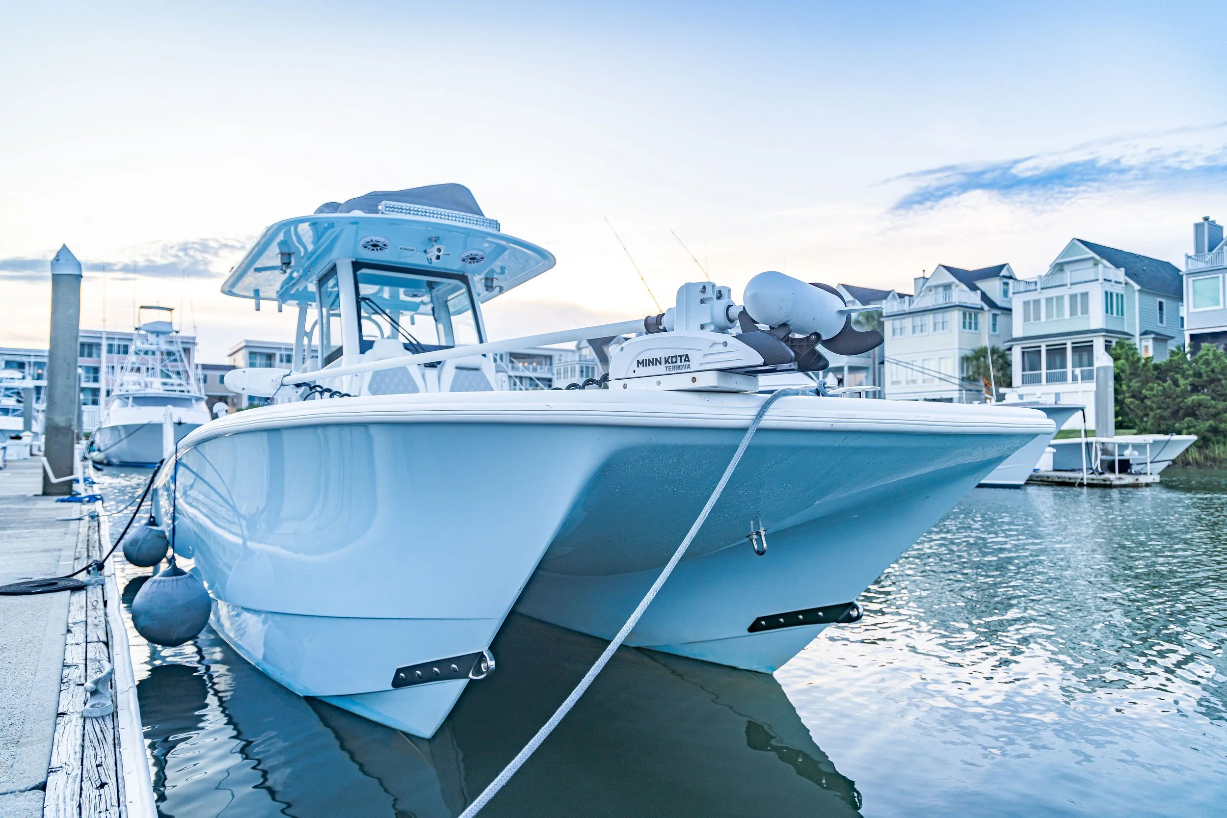 A white motorboat docked at a marina with apartment buildings in the background during sunset.