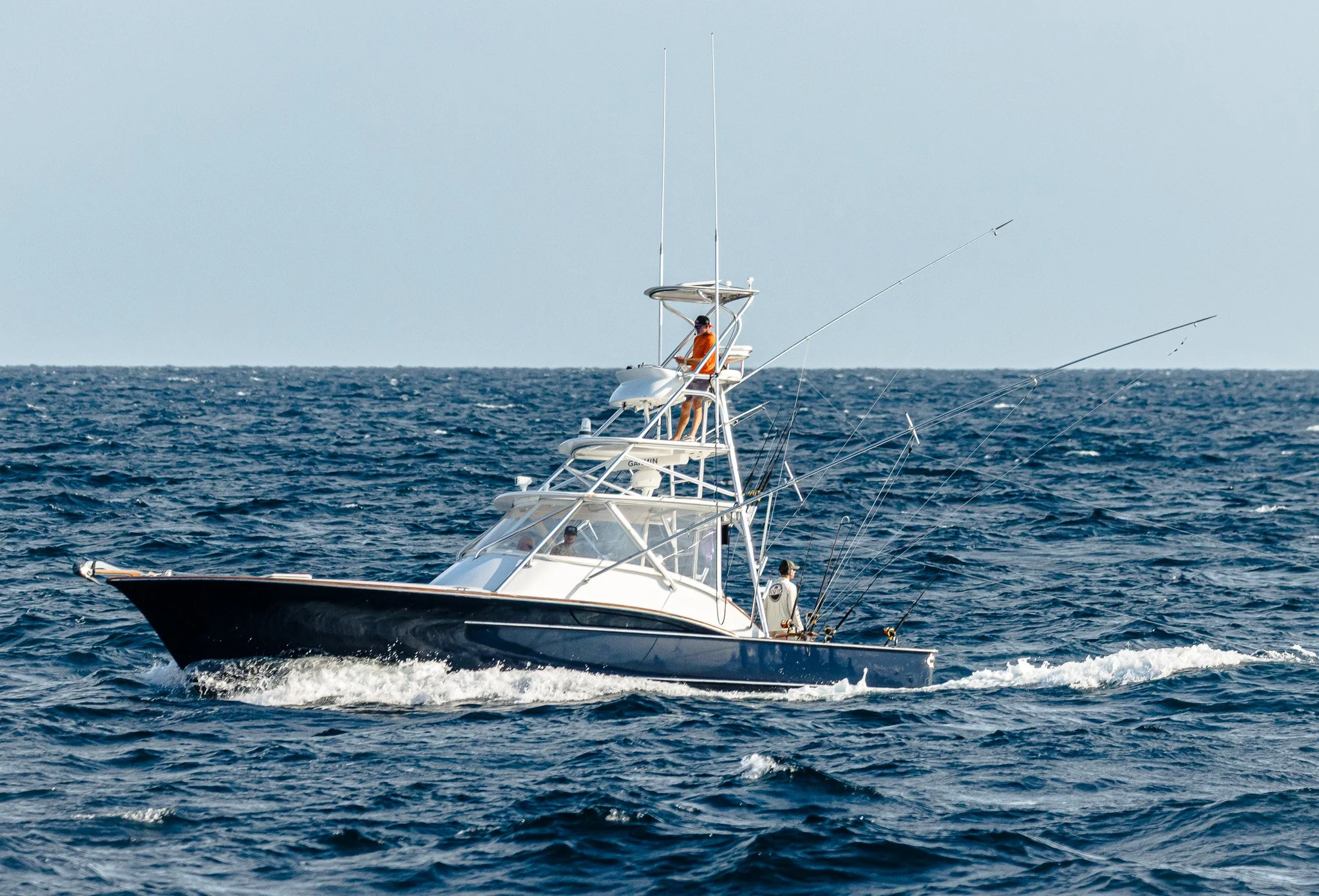 A white yacht with people on board sailing on the ocean, with fishing rods extended over the water.