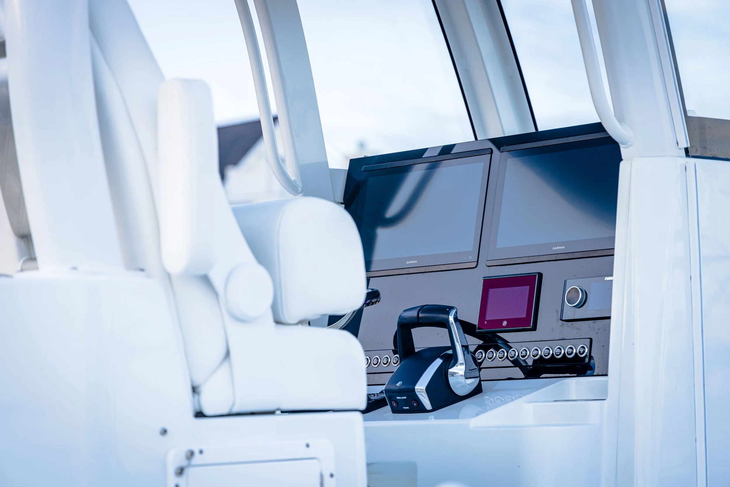 Close-up of a vessel's control panel with multiple digital displays and a throttle lever, interior of a modern boat with large windows showing blue sky and clouds outside.