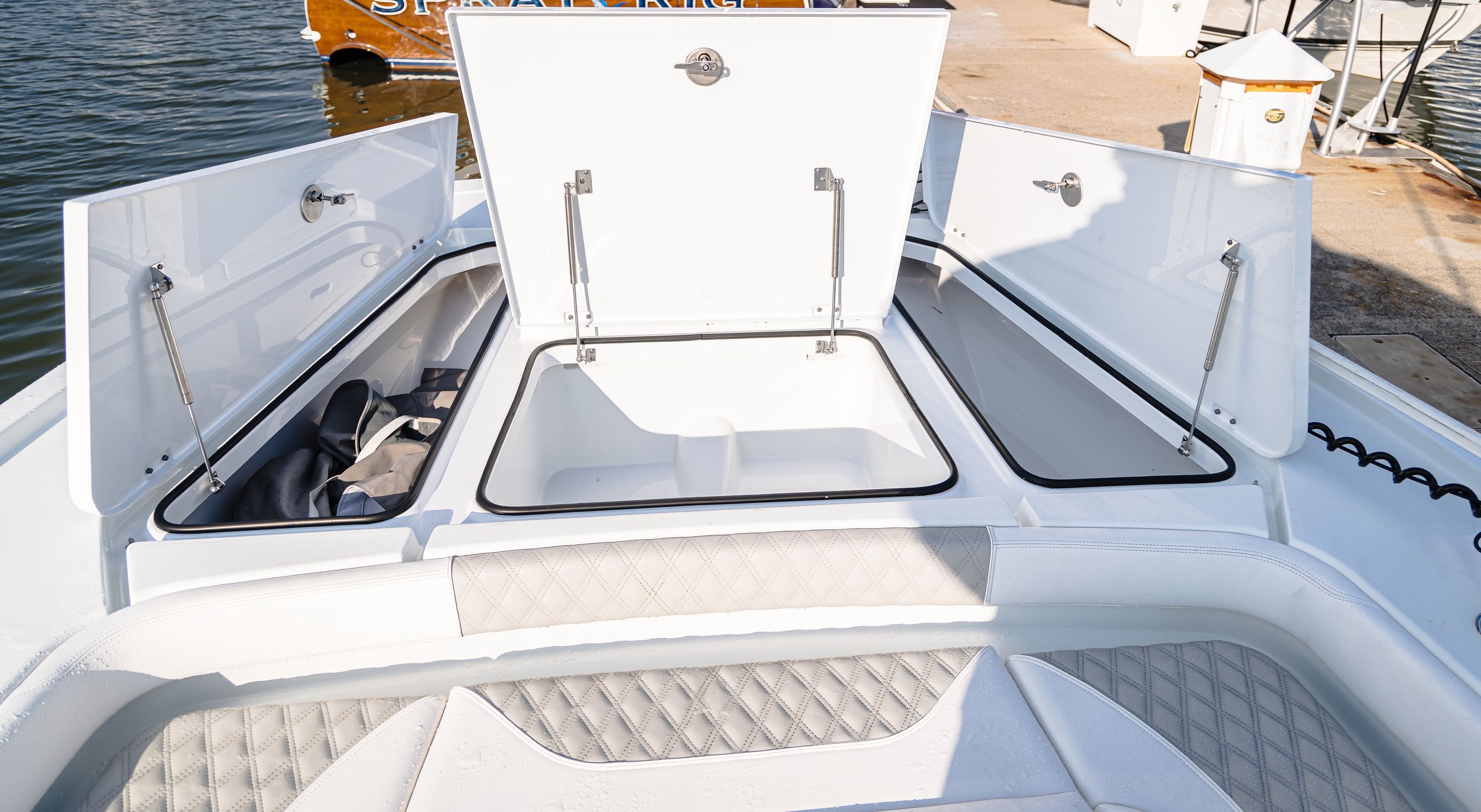 Open storage compartments on a white boat, with water and dock in the background.