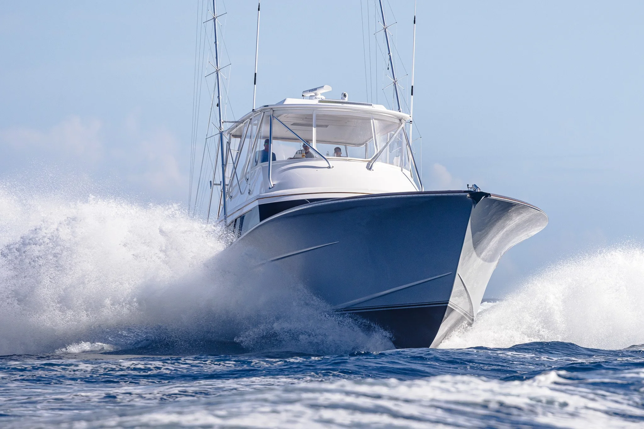 A white yacht cruising on the ocean, creating waves and spray in the water beneath a clear blue sky.