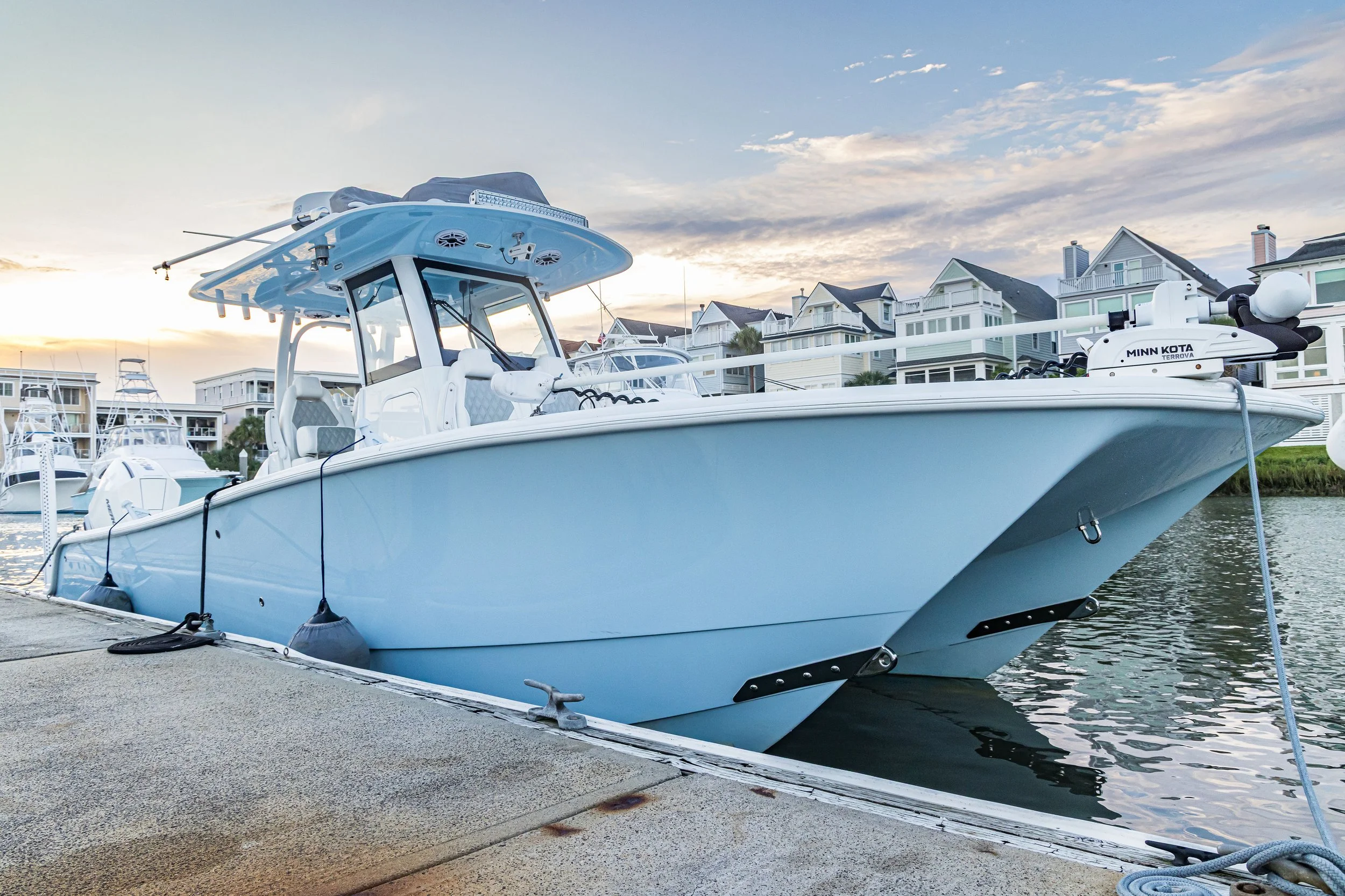 A white boat docked at a marina with homes in the background during sunset.