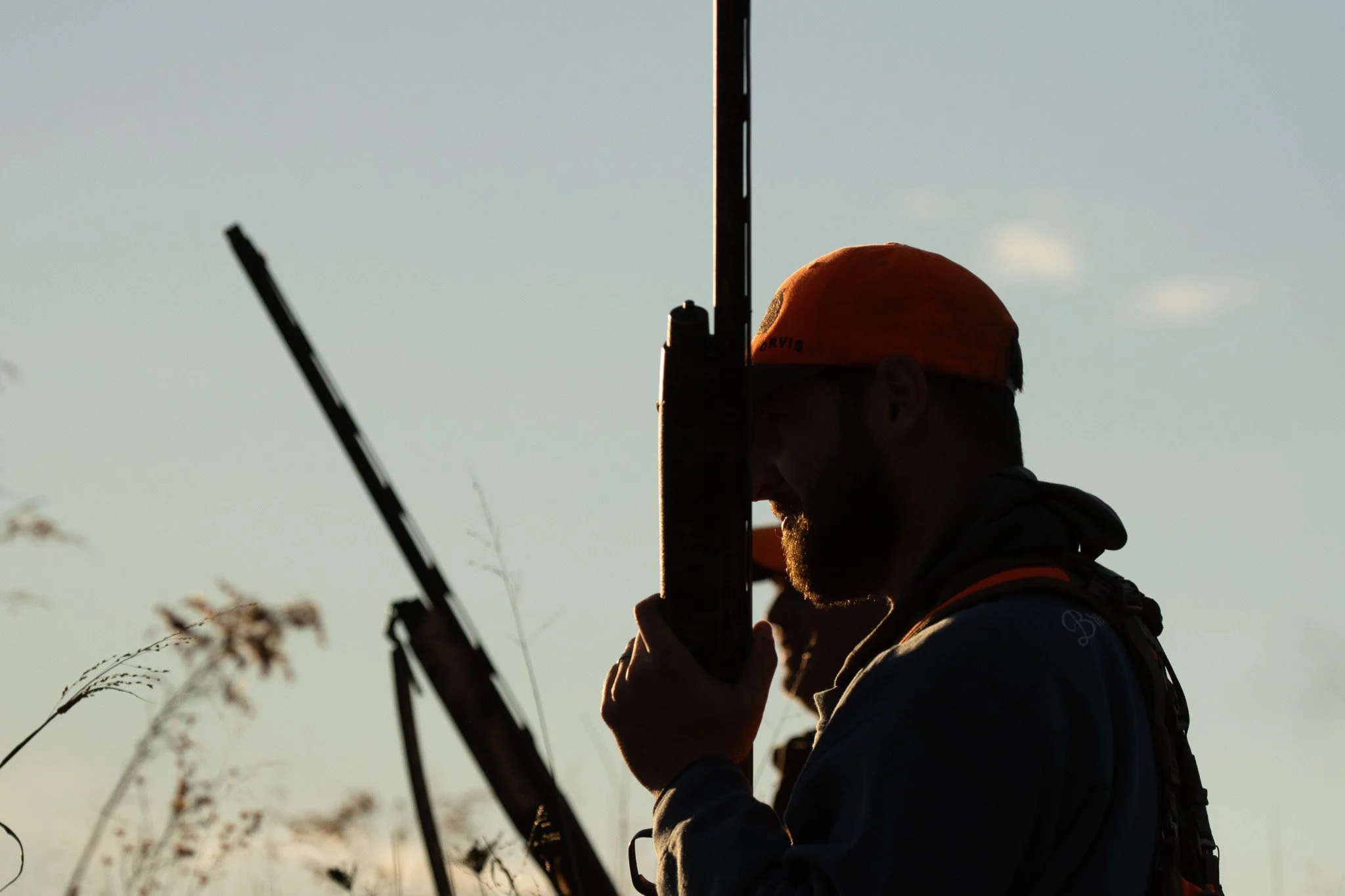 Silhouette of a person wearing an orange cap and holding a fishing rod against a clear sky during sunset.