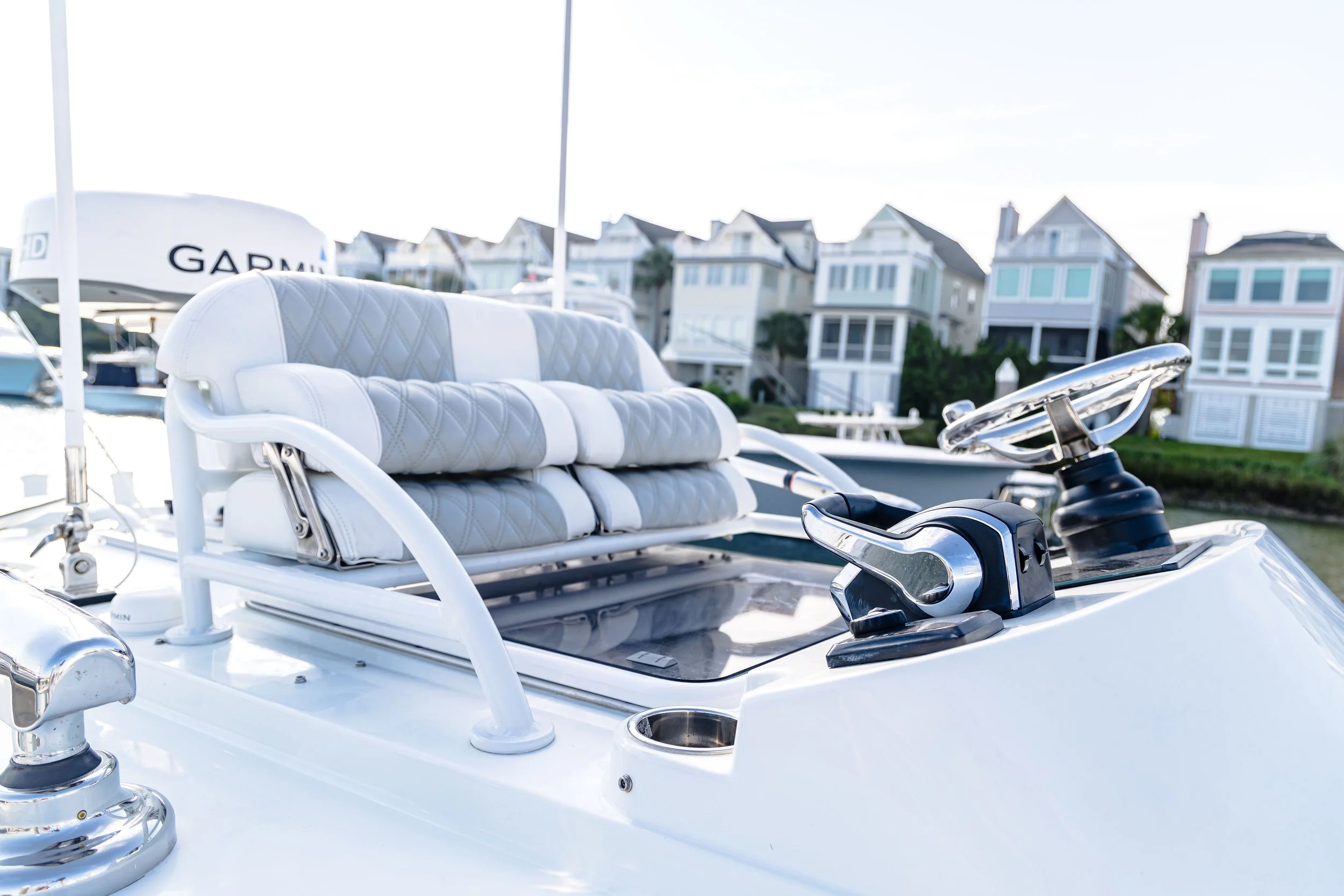 A white boat with a cushioned seating area and a Garmin GPS device, docked near multi-story beach houses.