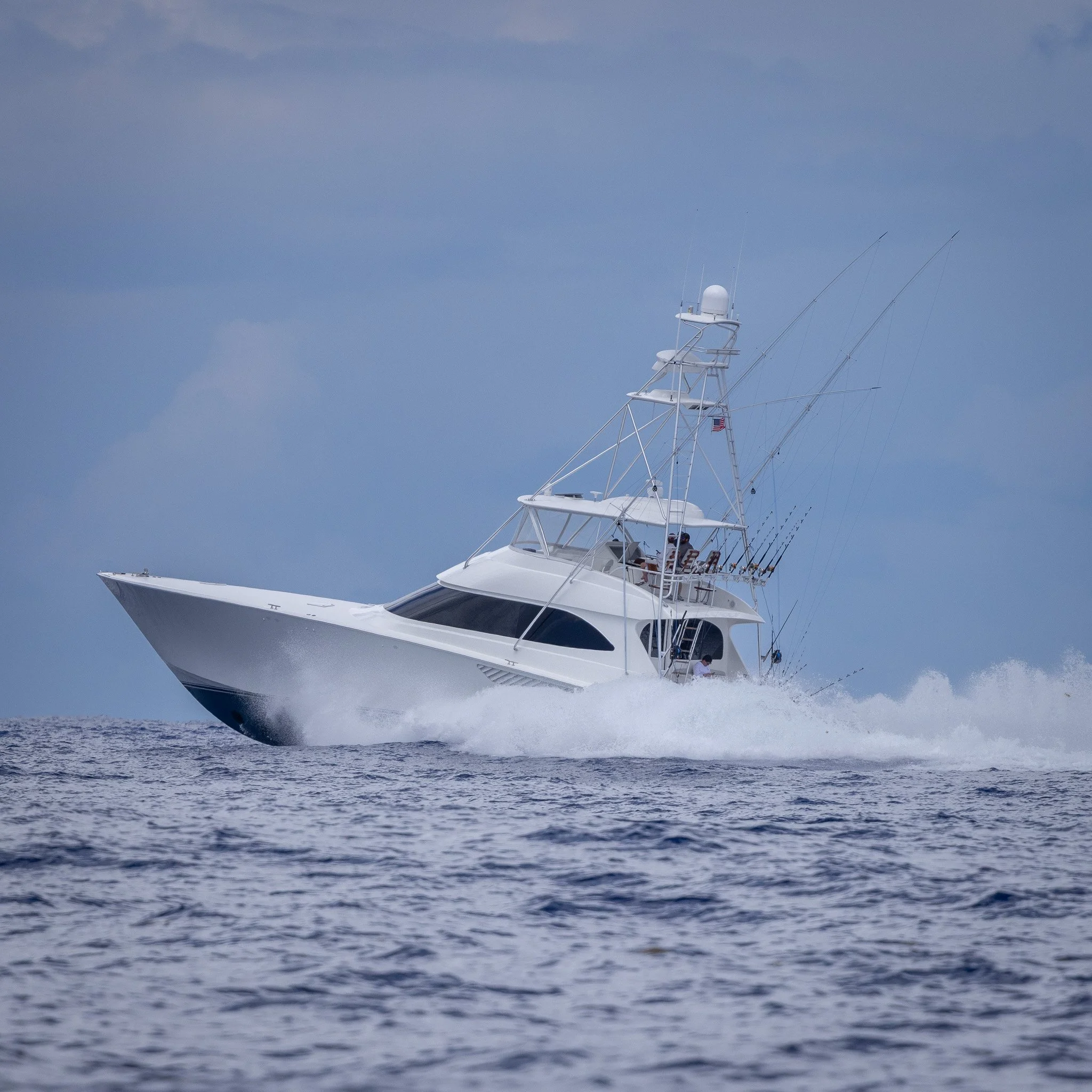 A large white yacht moving at high speed on the water with a clear blue sky above.