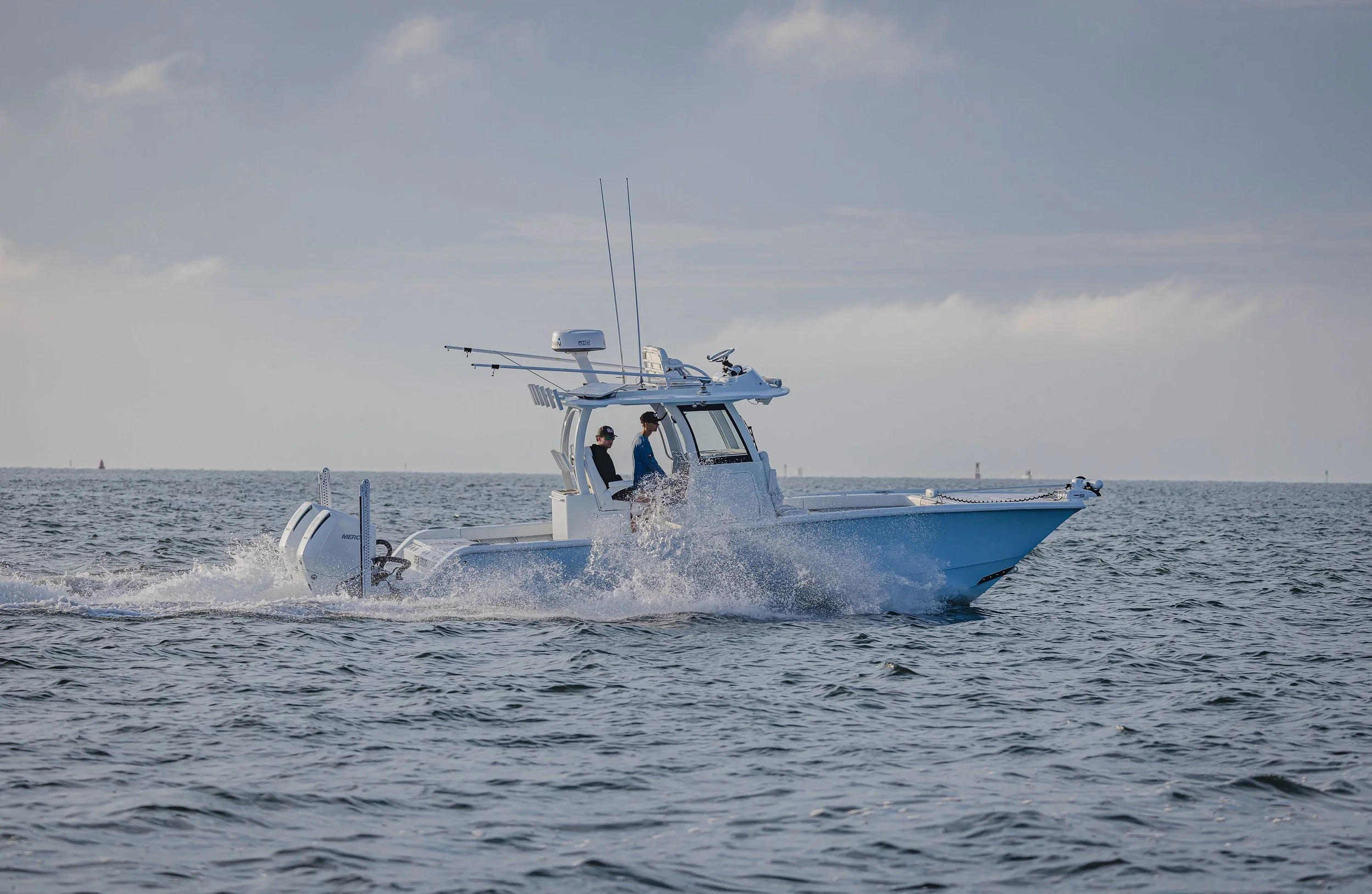 A white speedboat with two people on board, speeding across open water under a partly cloudy sky.