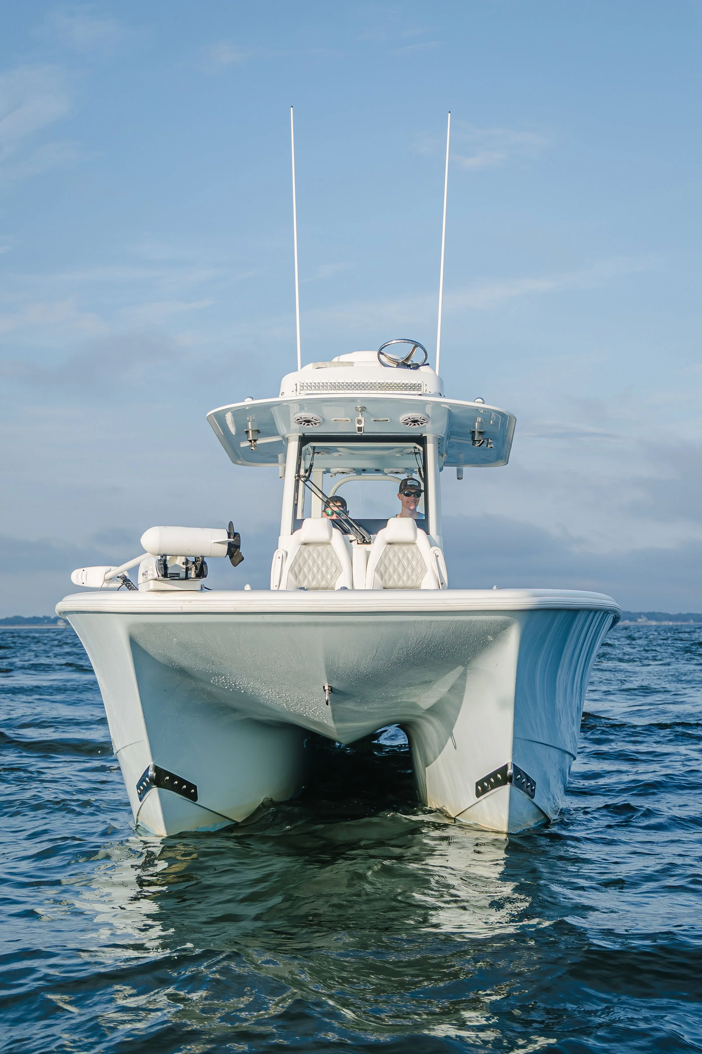 White yacht on the water with two men on board, under a blue sky with a few clouds.