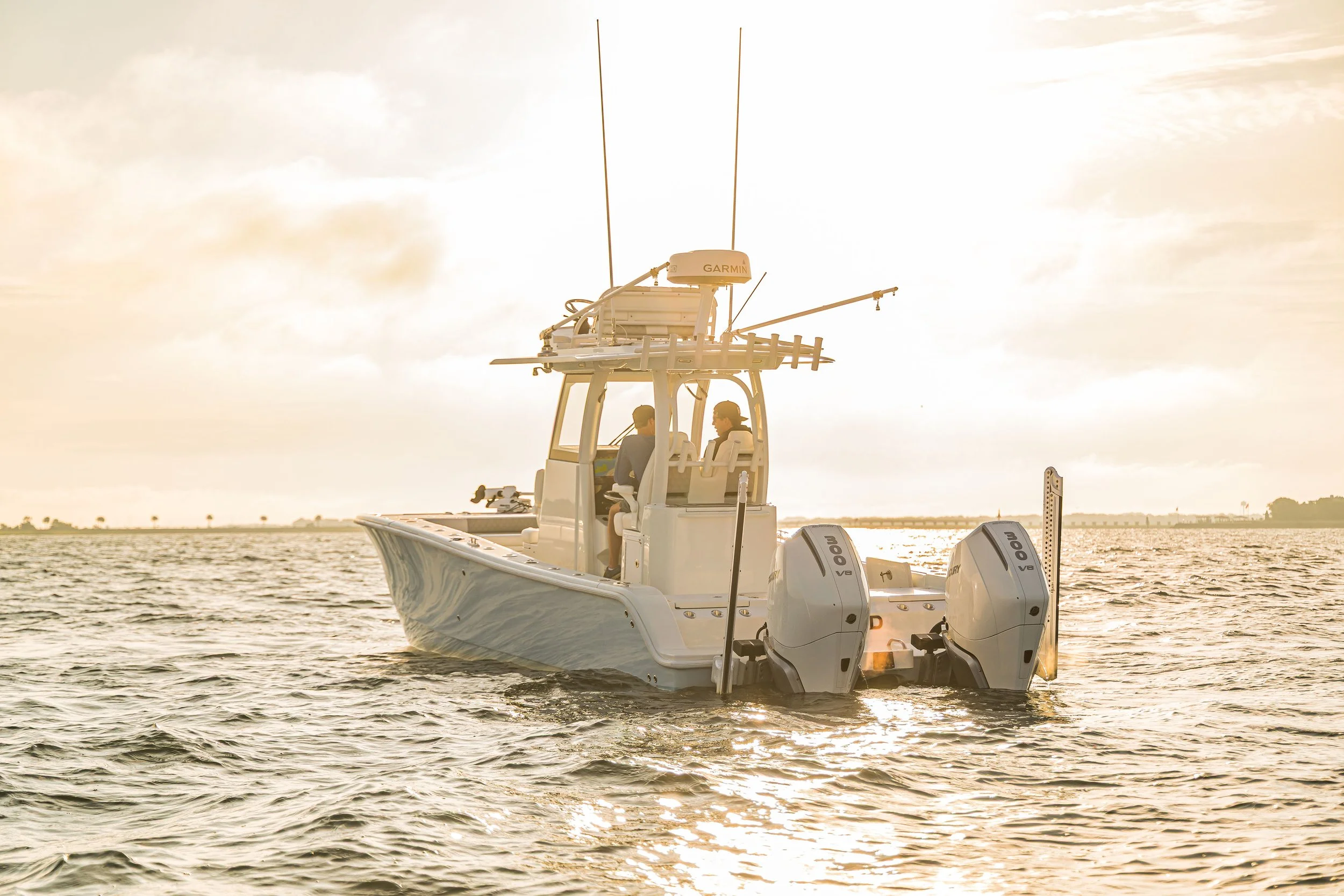 A motorboat with four outboard engines is floating on a body of water during sunset, with two people visible inside the boat's cabin.