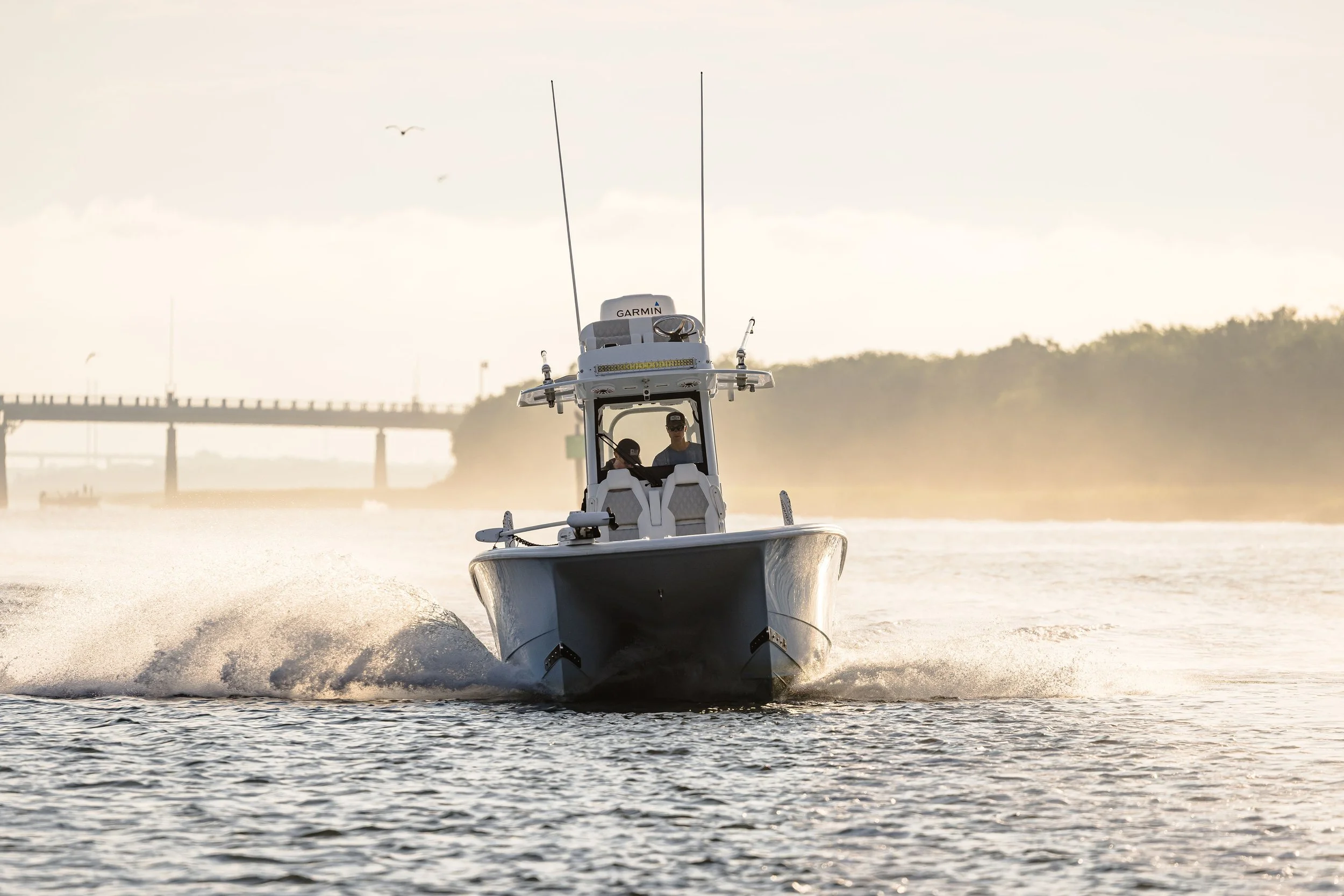 A small motorboat moving through water at sunset, with a person wearing sunglasses inside, and a Garmin radar on top.