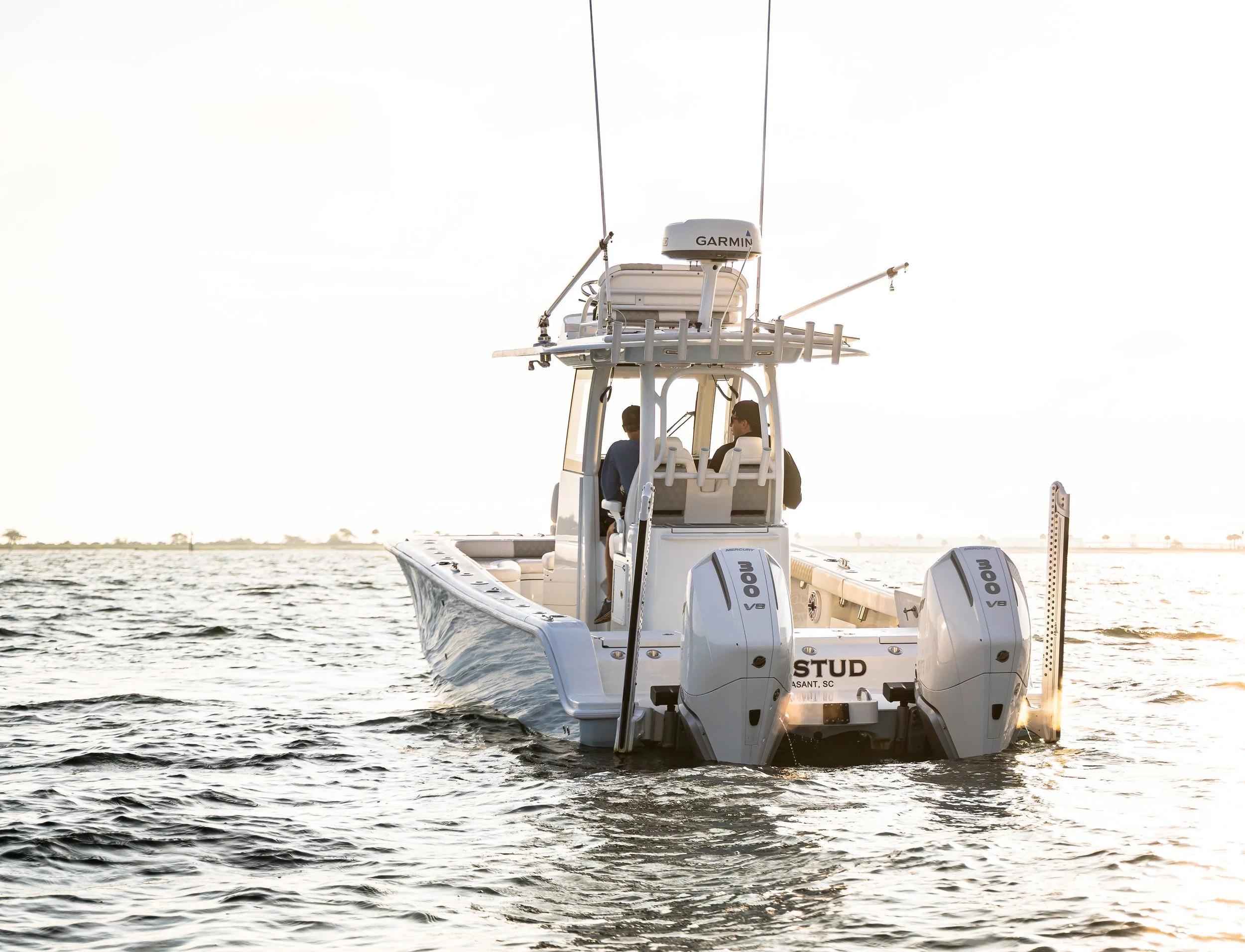 A white boat with twin outboard motors on water at sunset, with two people seated at the front of the boat facing each other.