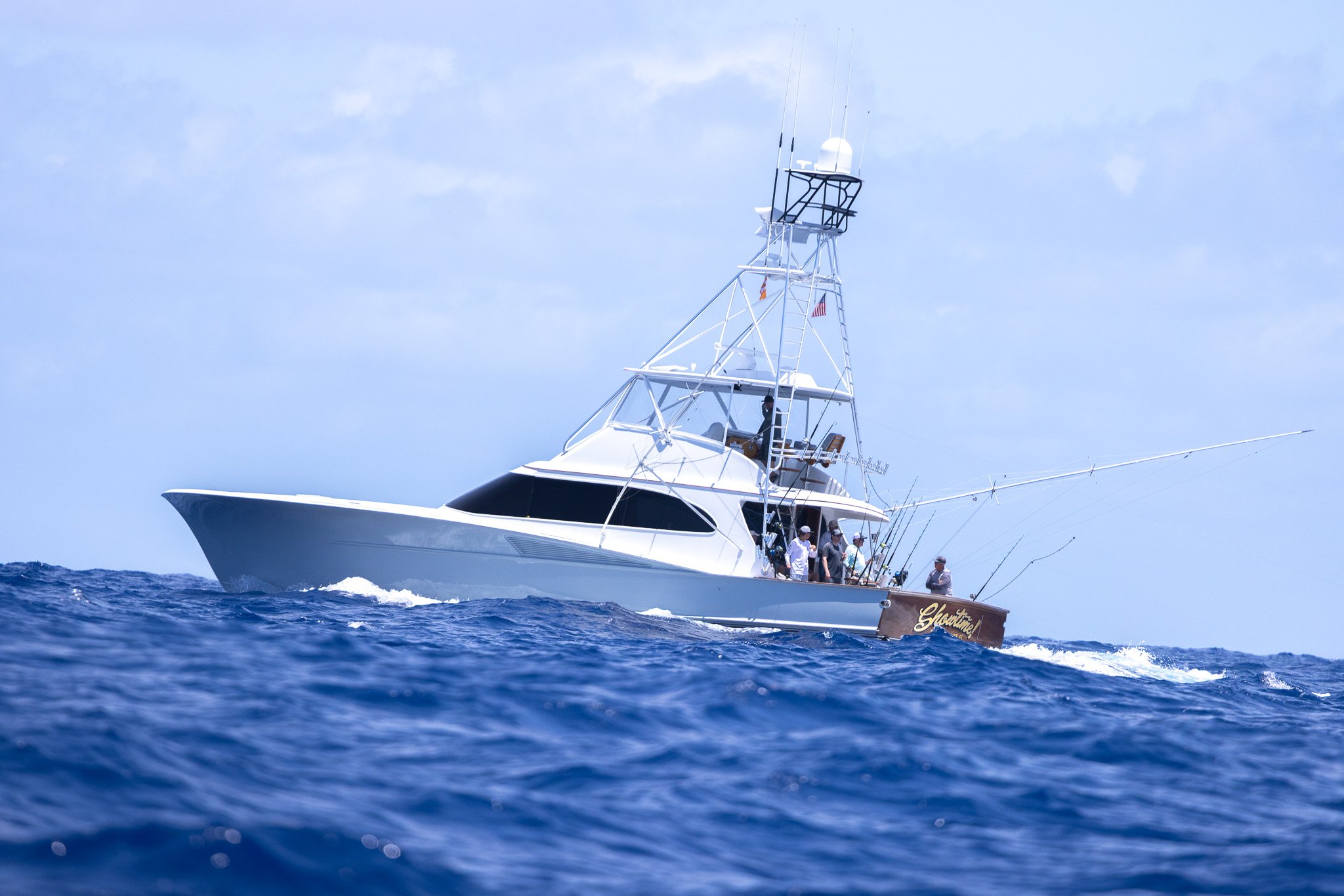 A group of people fishing from a white yacht named 'Elysian' sailing on blue ocean waters under a partly cloudy sky.