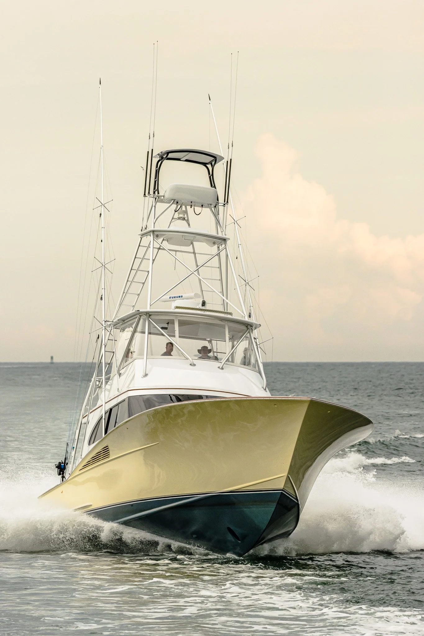 A large motorboat speeding on the ocean, with a clear sky and some clouds in the background. The boat has a white and black color scheme, with a tall flybridge and antennas.