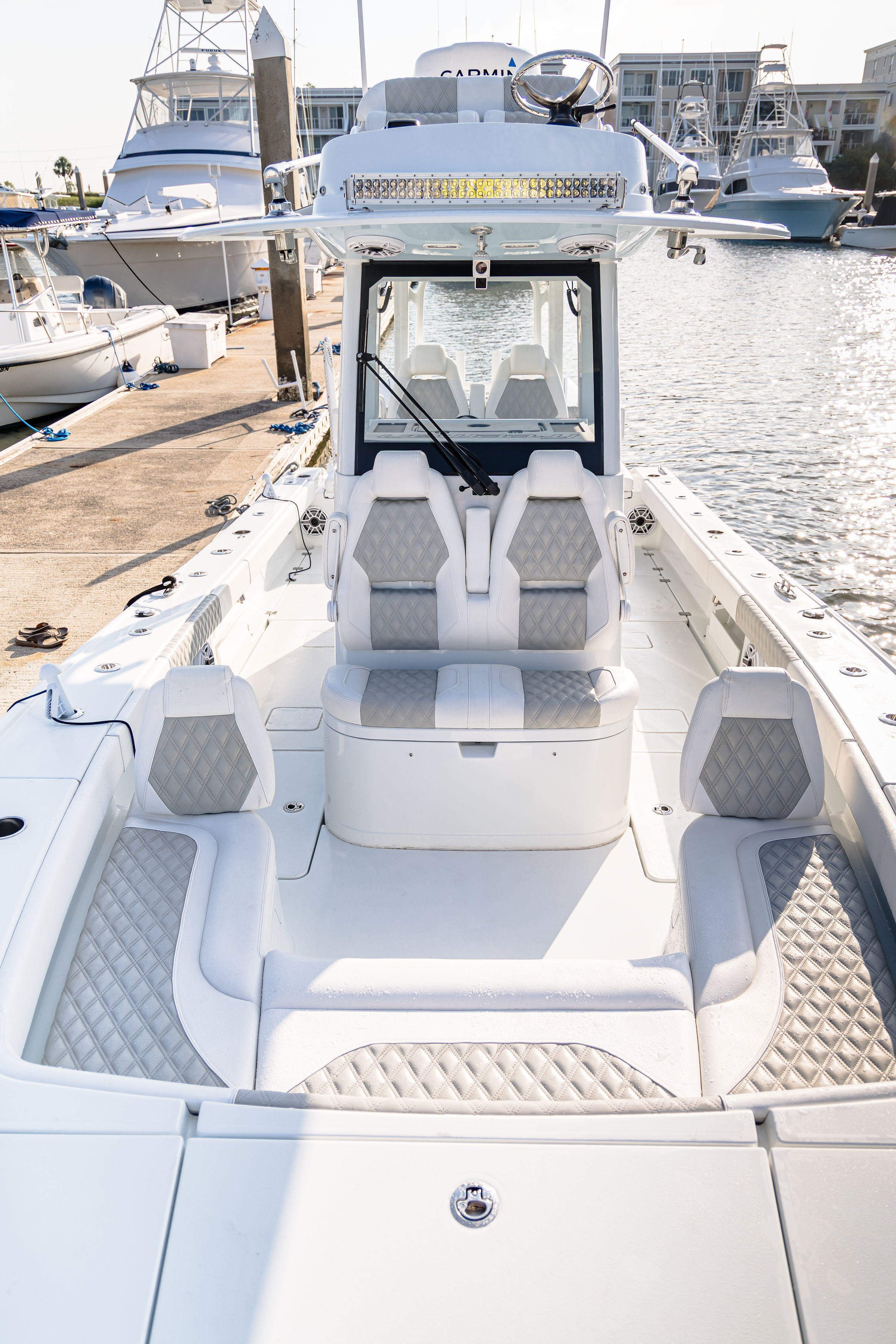 View of the bow of a white luxury boat docked at a marina, featuring cushioned seating with quilted patterns and surrounded by other boats and yachts.