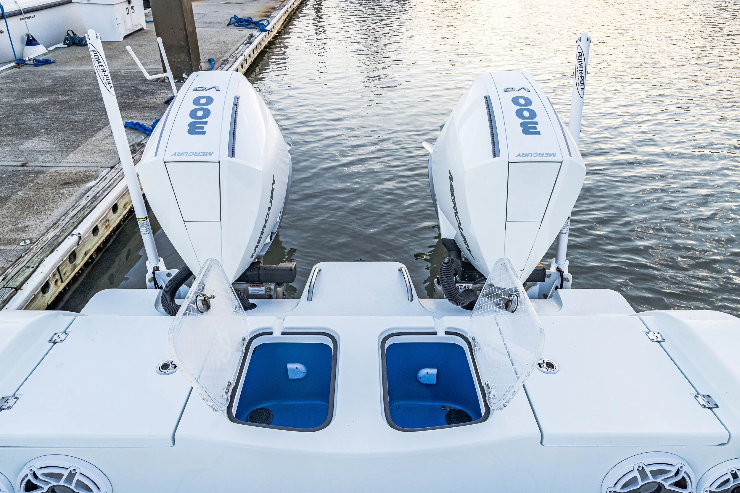Two white outboard motors mounted on the back of a boat at a dock, with the water reflecting the sky and a wooden dock on the left side.