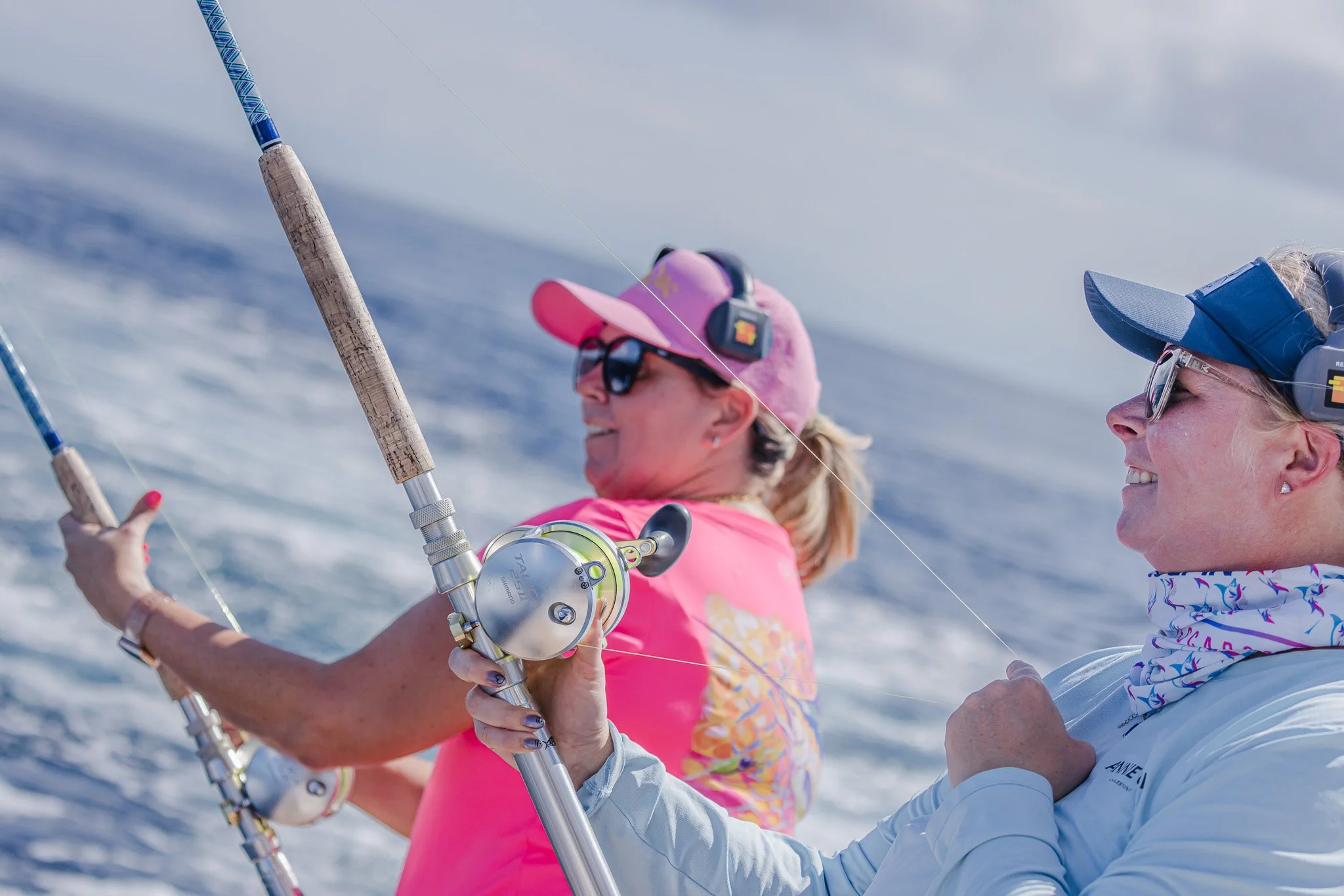 Two women in sunglasses and hats are fishing together on the water, smiling and enjoying their day.