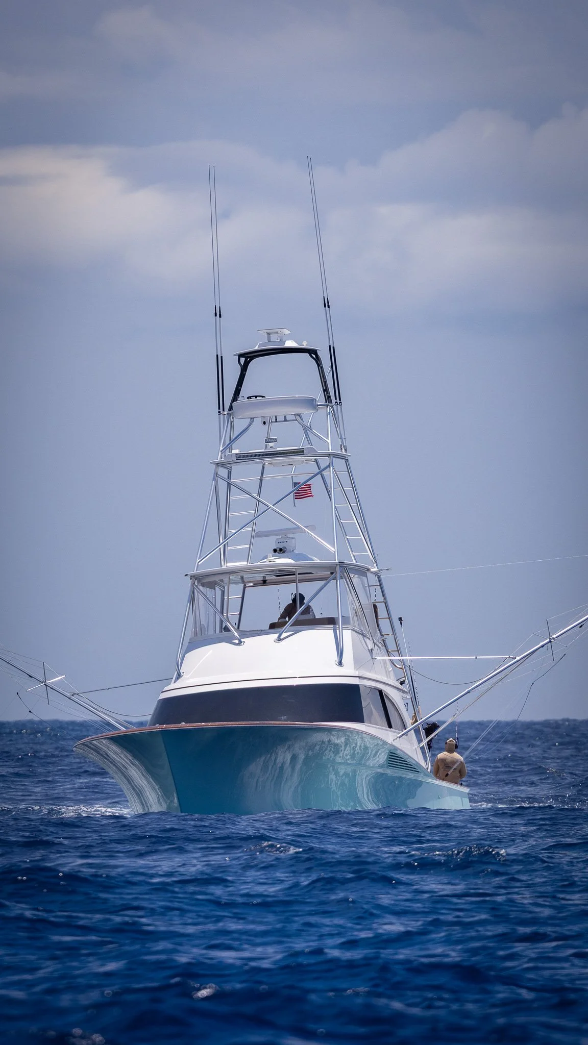 A sailboat on the water with a man standing on the deck, under a partly cloudy sky.
