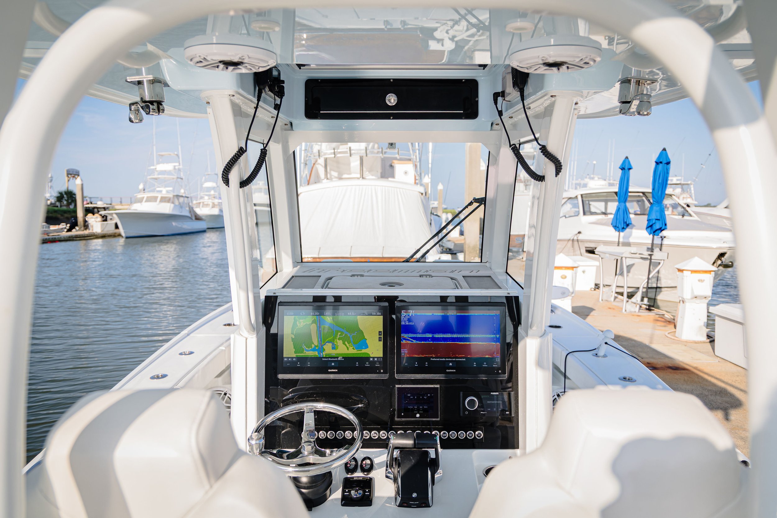 View from the cockpit of a boat showing navigation and fishfinder screens, with a marina and boats in the background.