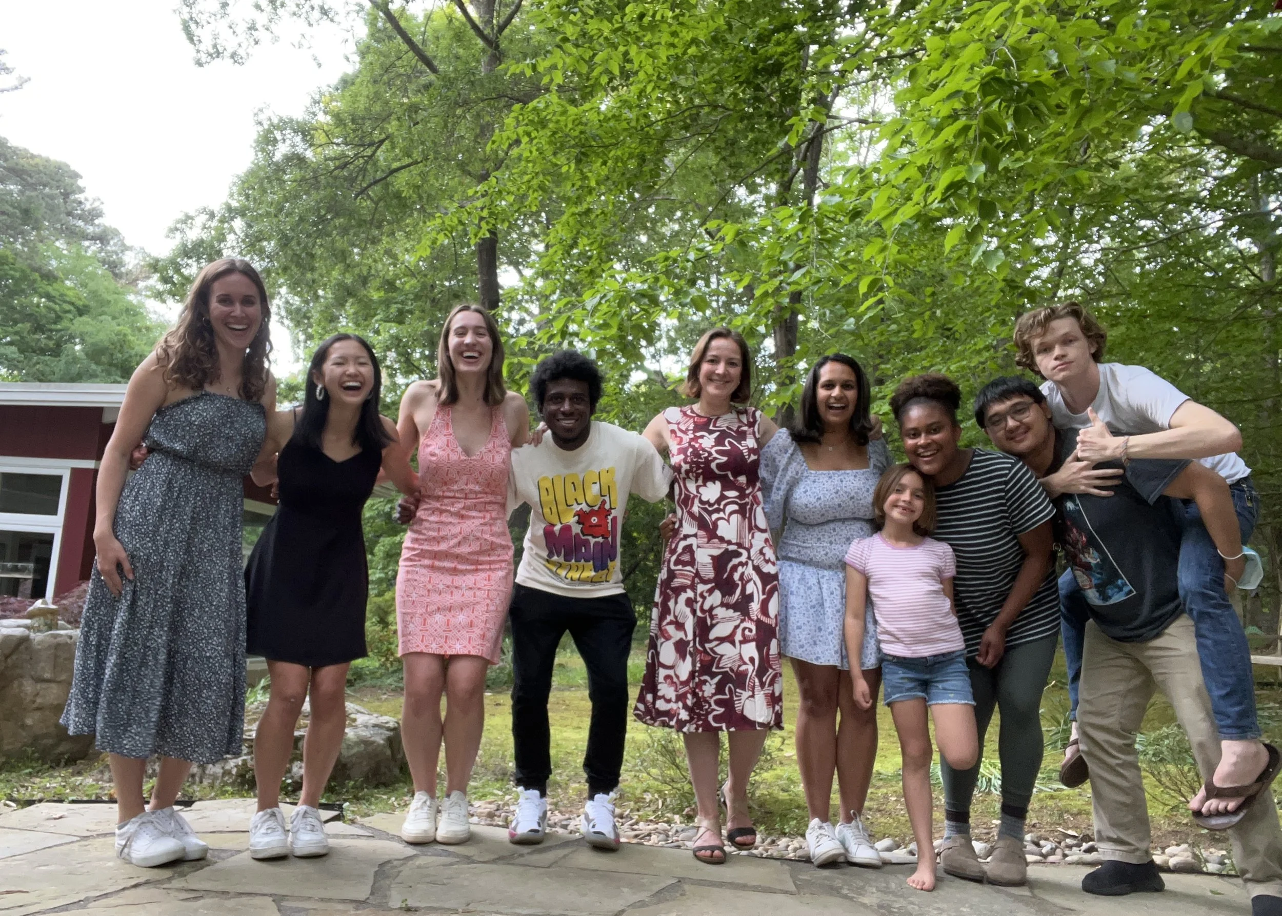 Group of nine diverse young people smiling and posing together outdoors under trees