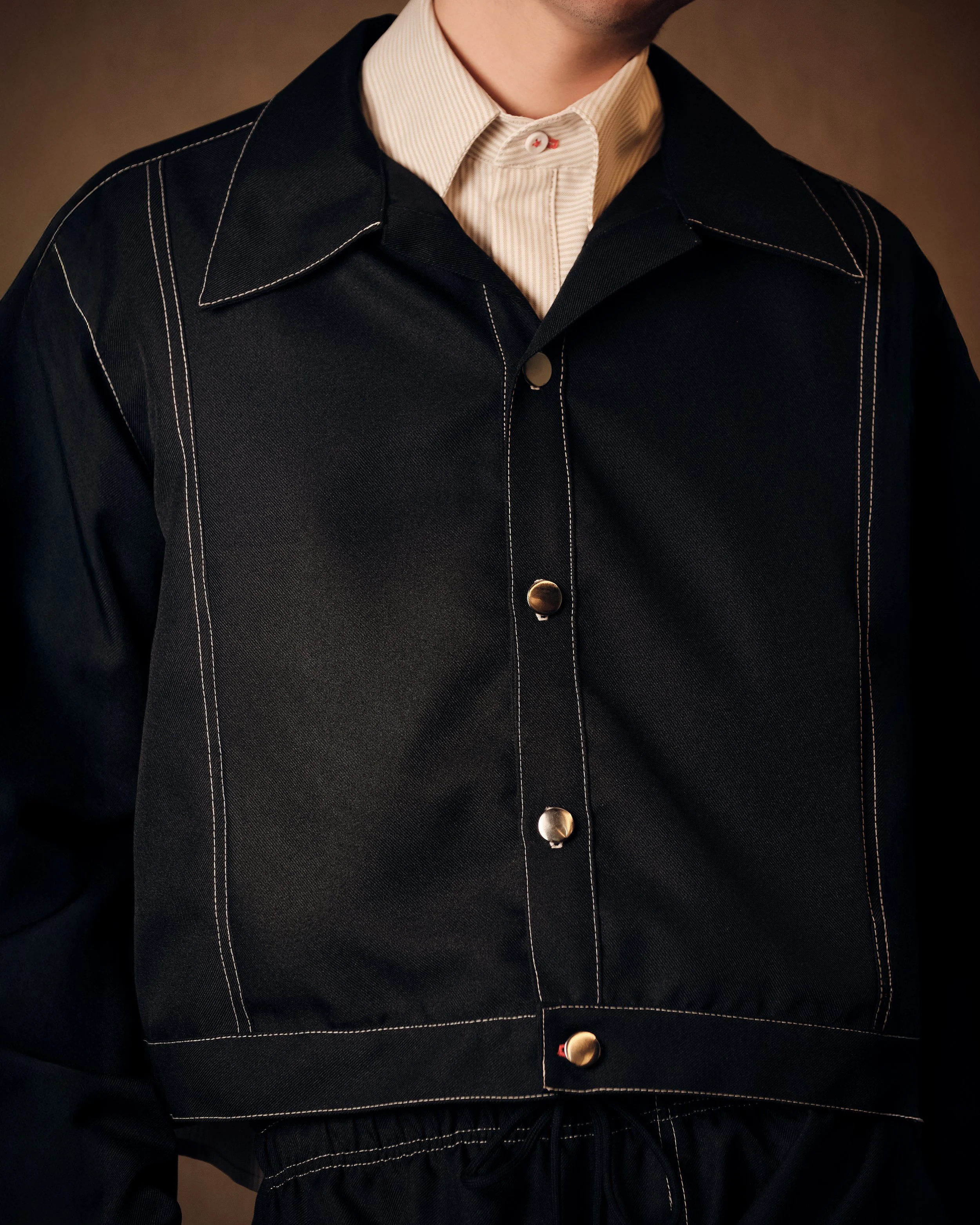 Imagen de una persona usando una chaqueta negra con costuras blancas, con una camisa blanca debajo.